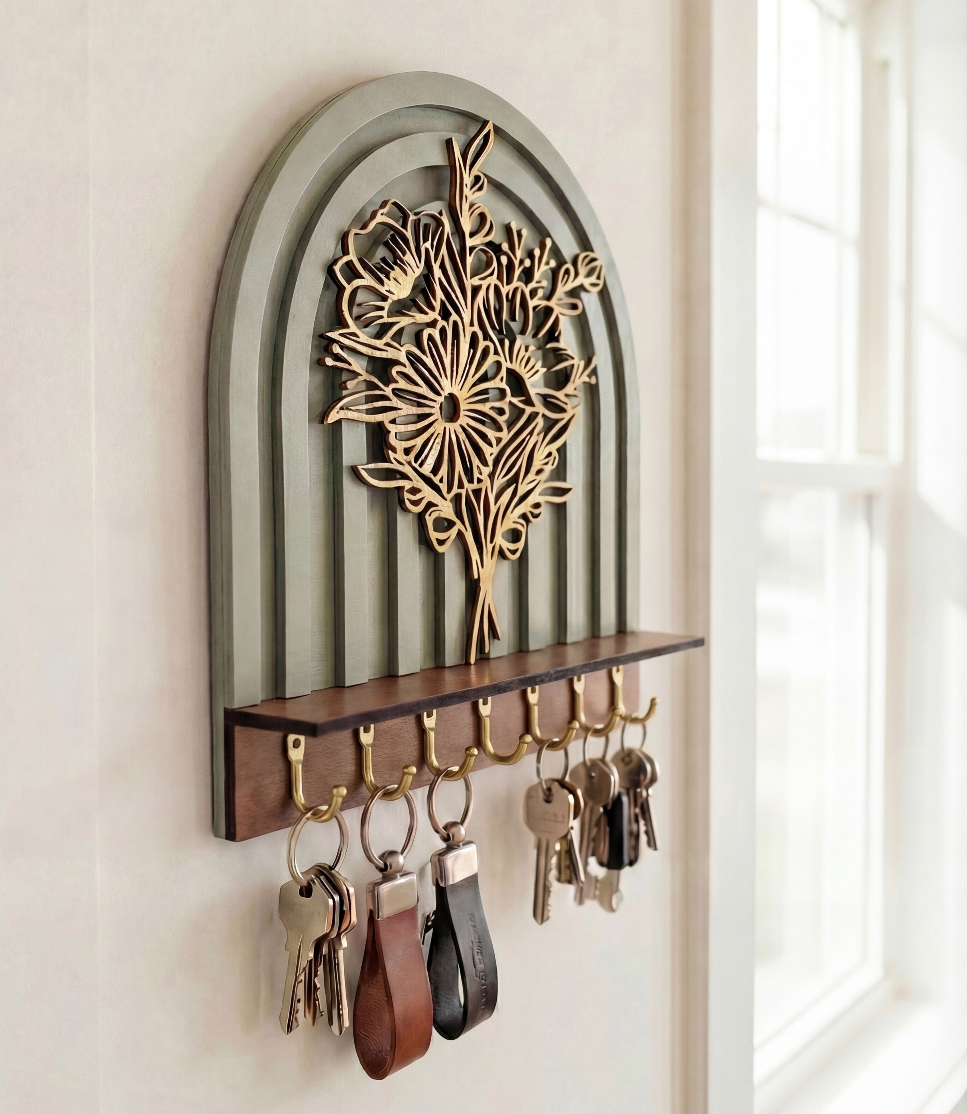 Arched wall-mounted key holder with layered botanical floral design and brass hooks holding keys