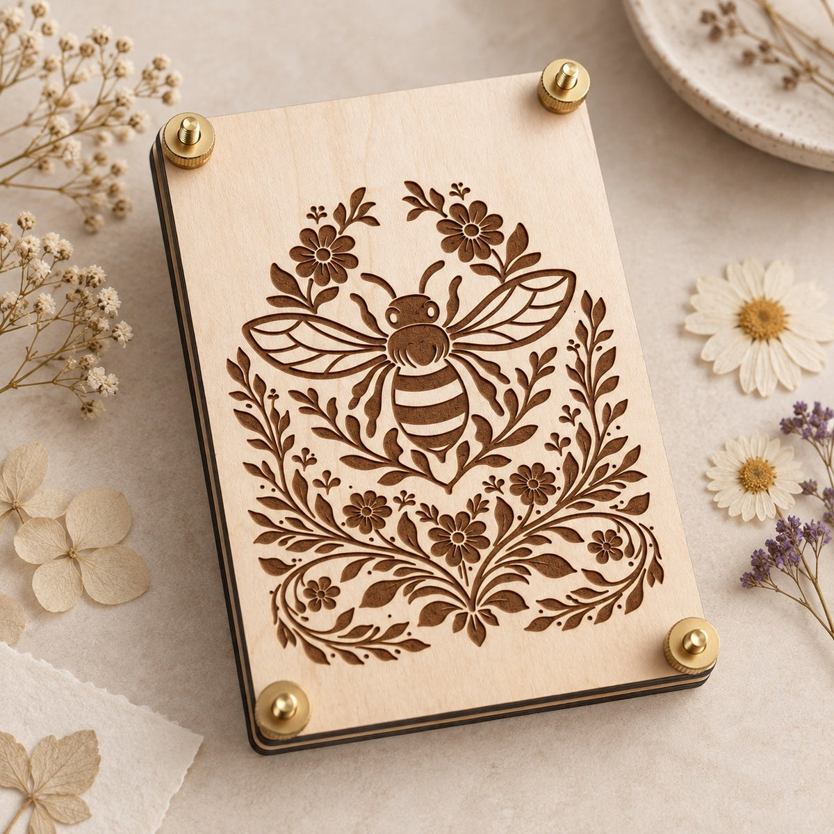 Wooden bee flower press with floral laser engraving and brass hardware styled with delicate dried flowers on a soft neutral background.