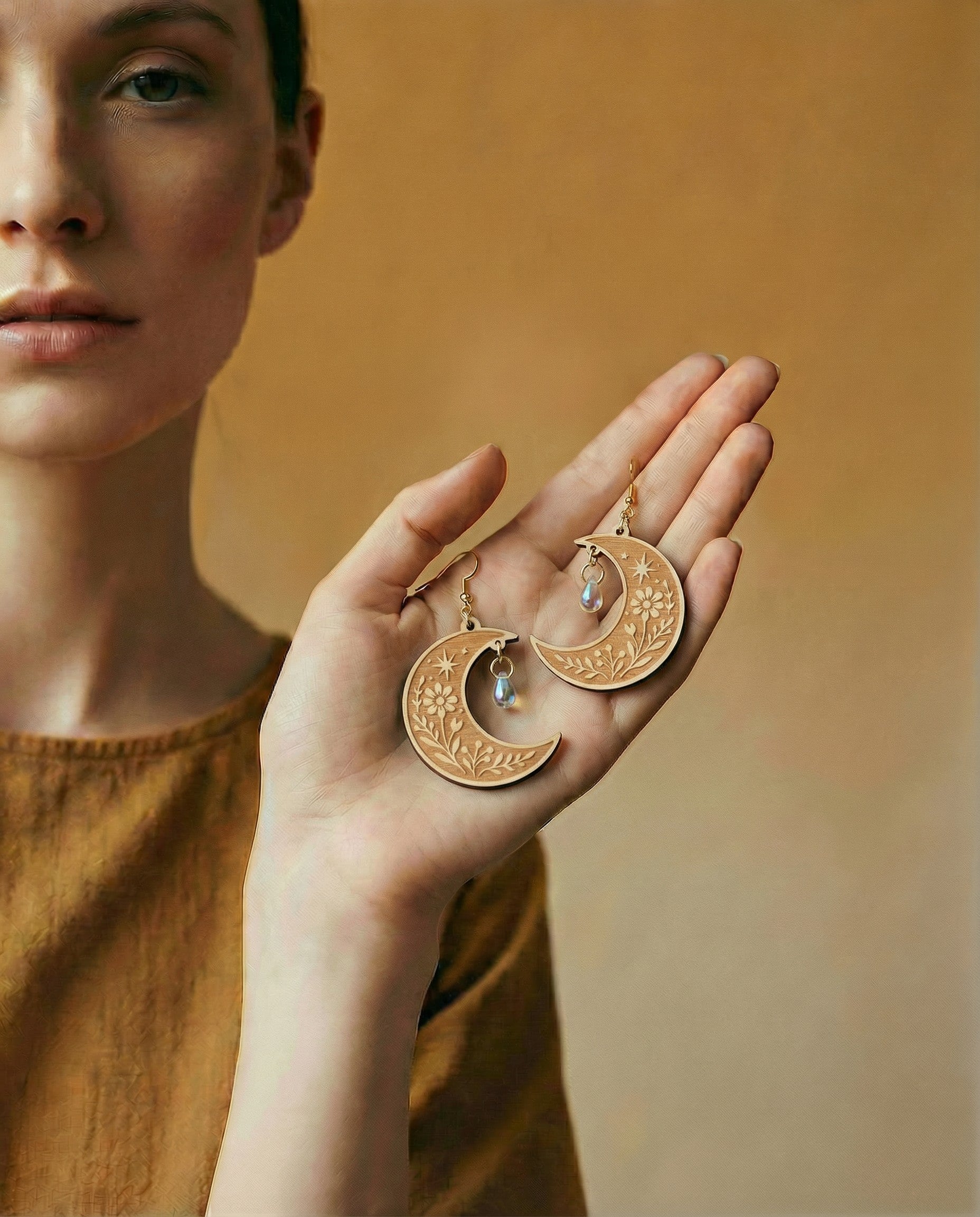 Woman holding wooden crescent moon earrings with a warm background
