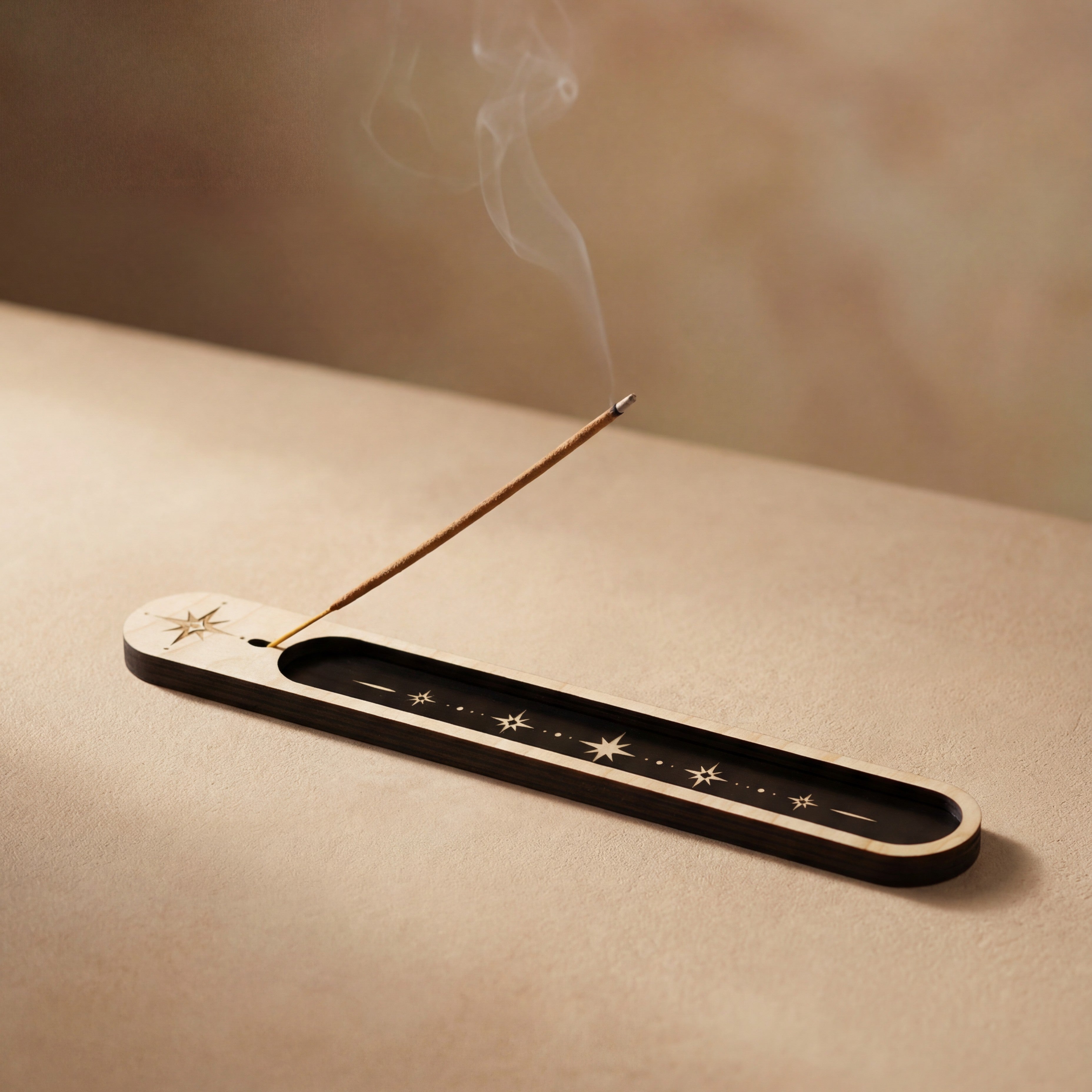 Lit incense stick resting in a slim wooden incense holder with a black inlay and celestial star design, with smoke curling upward.