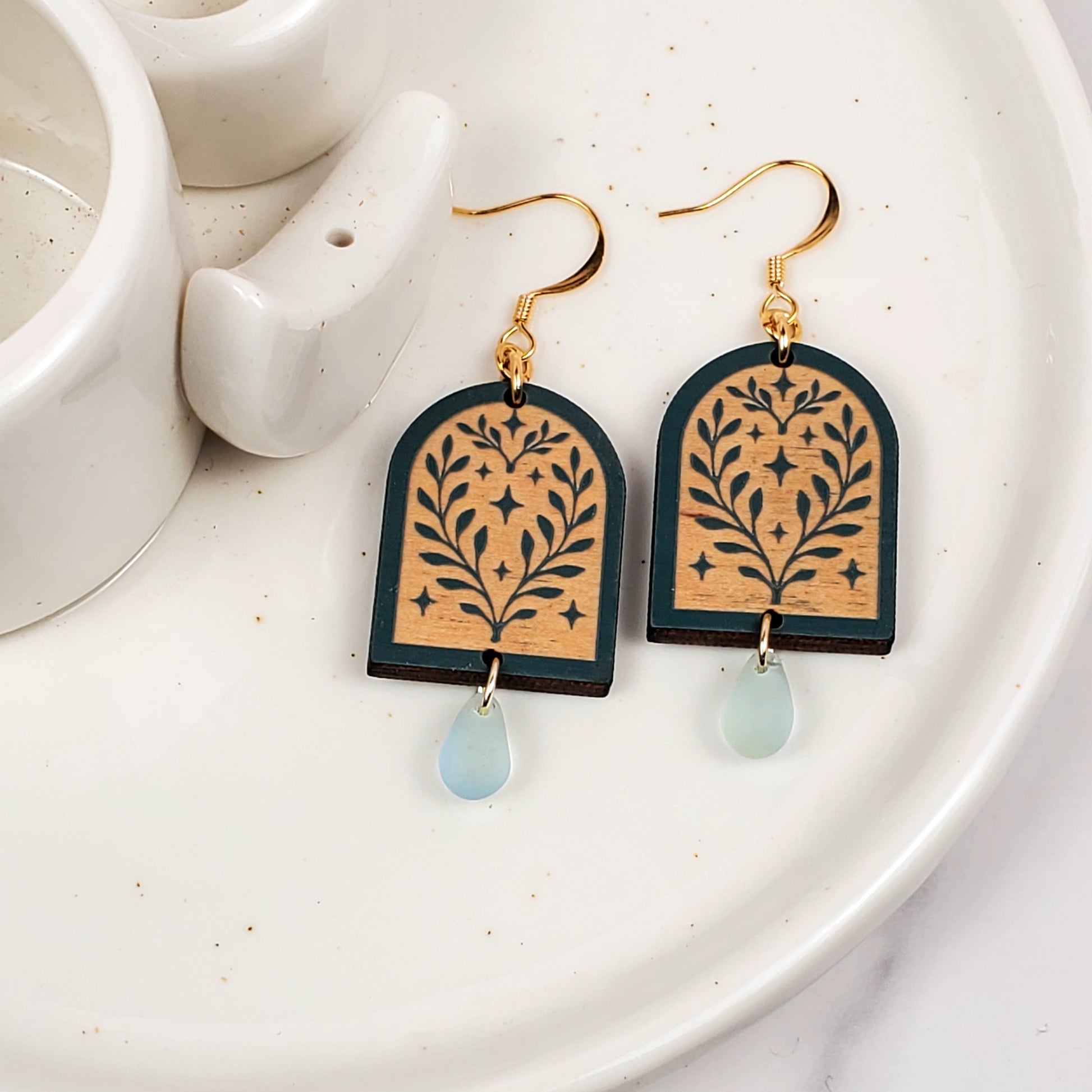 Decorative earrings with floral design and light blue teardrop on a white plate.