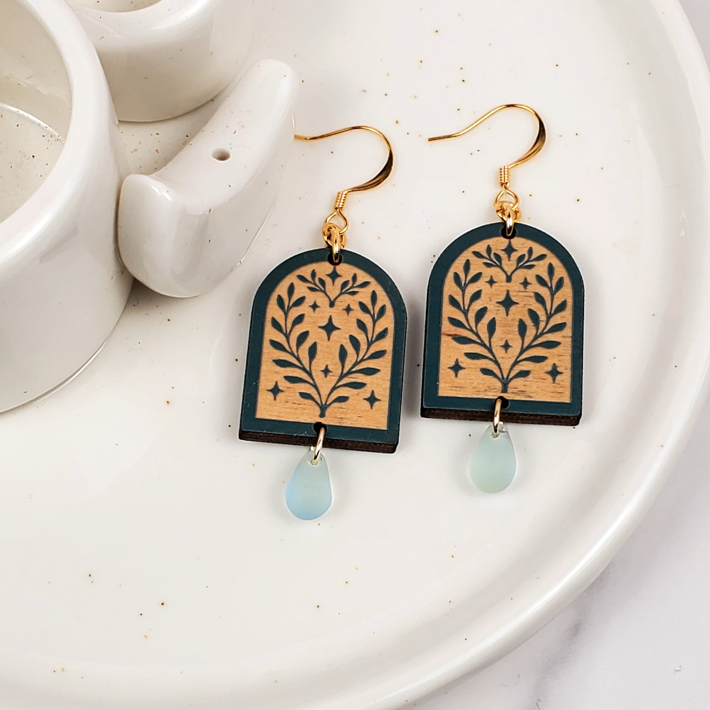 Decorative earrings with floral design and light blue teardrop on a white plate.