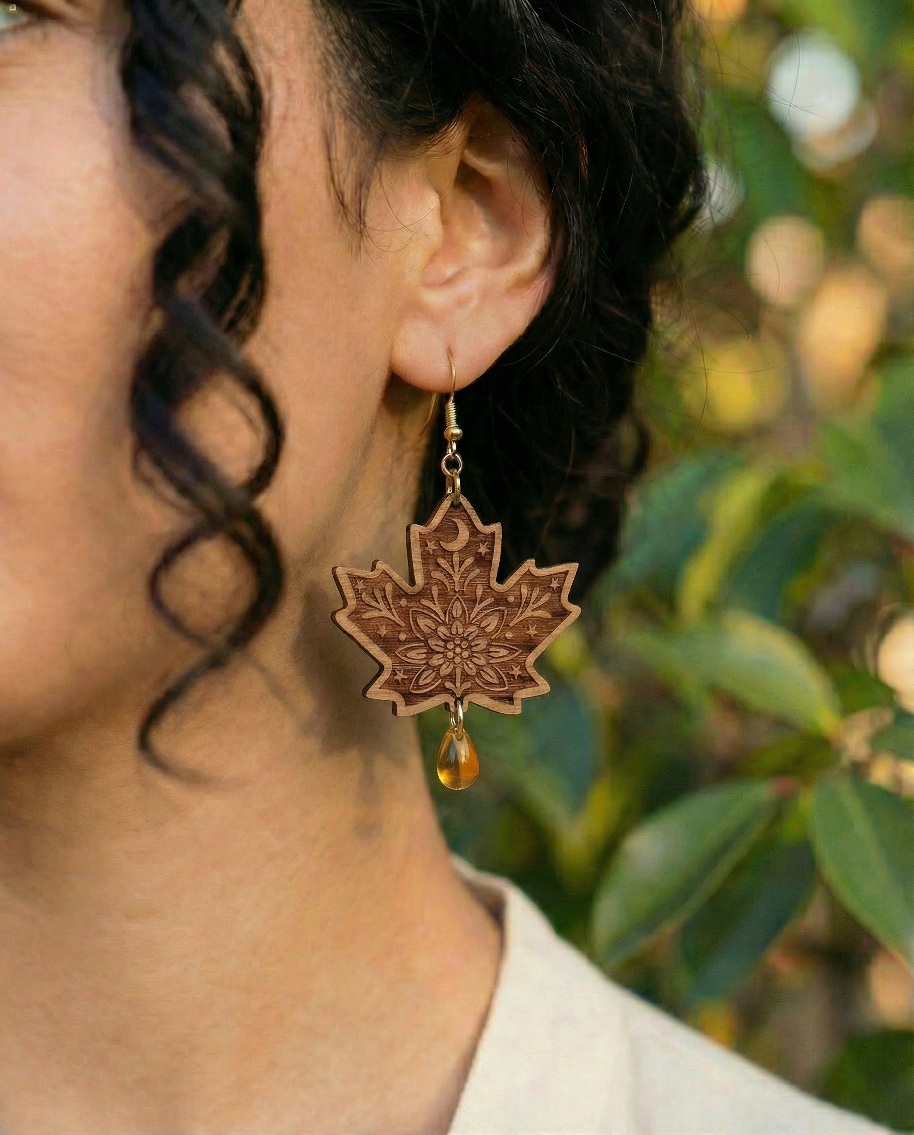 Model wearing engraved maple leaf wood dangle earring with amber Czech glass teardrop bead and 14k gold hook.