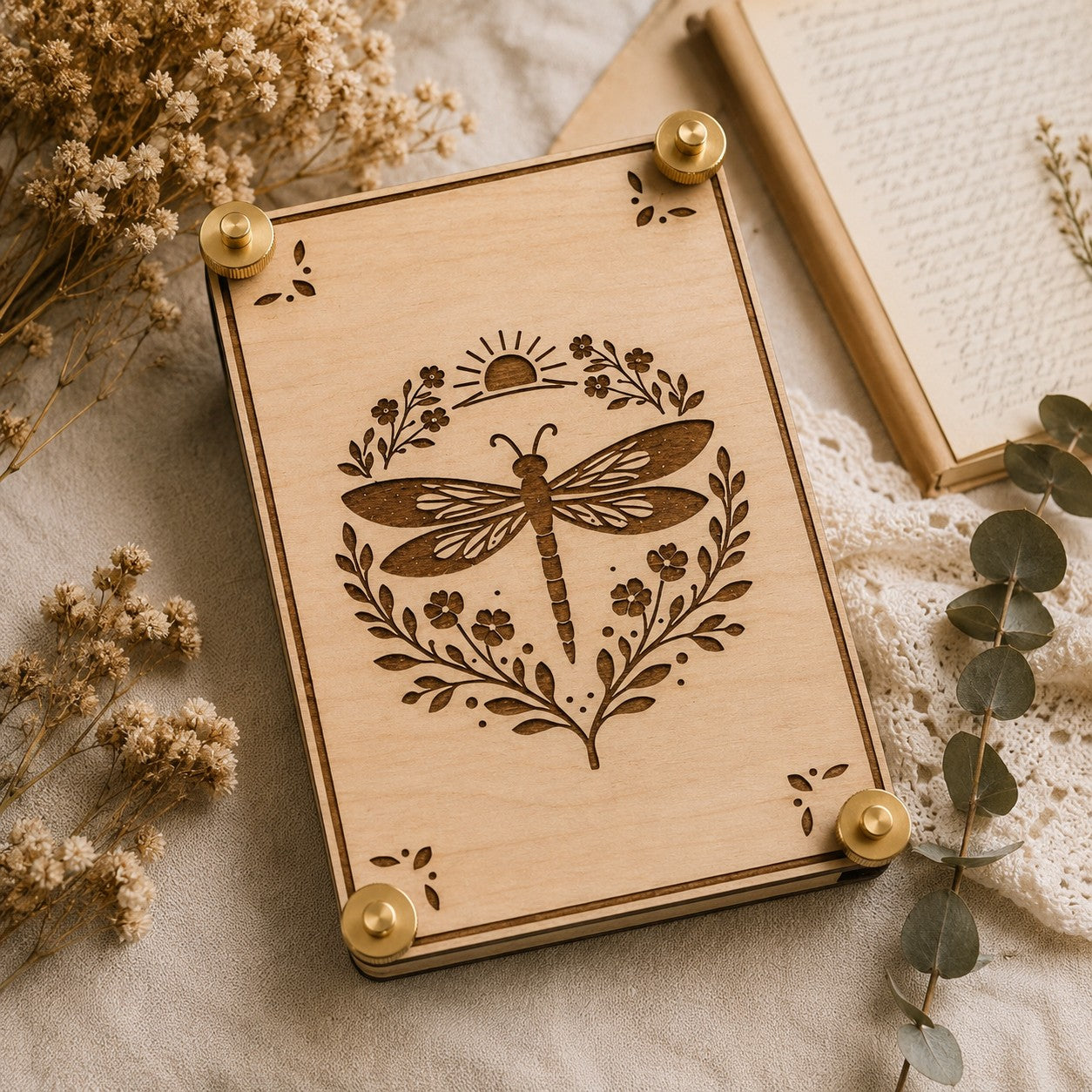 Handmade wooden flower press with laser-engraved celestial dragonfly botanical design, brass hardware, styled with dried wildflowers and eucalyptus on linen