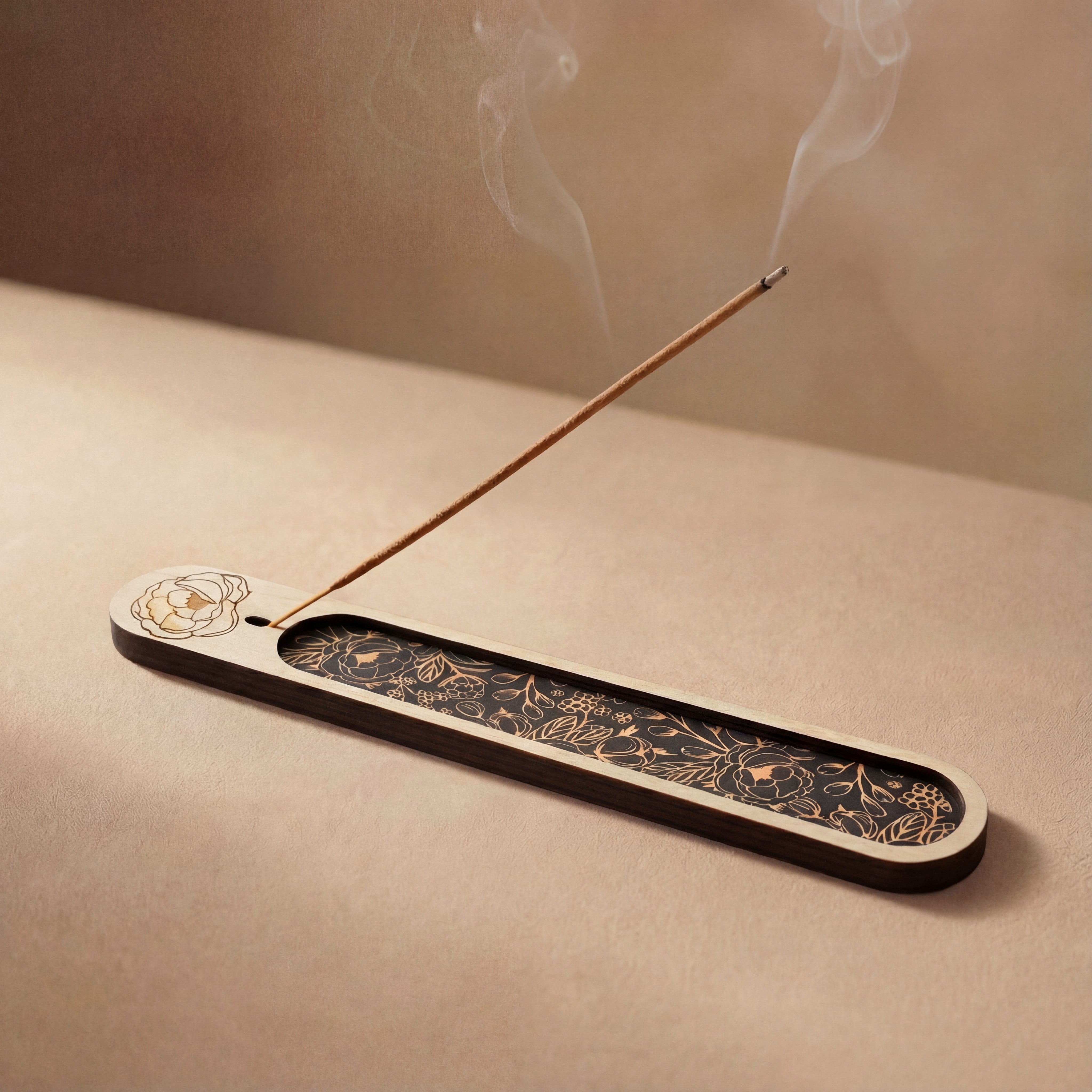 Wooden incense holder with a floral engraving and black botanical inlay, holding a lit incense stick with smoke rising on a neutral background.