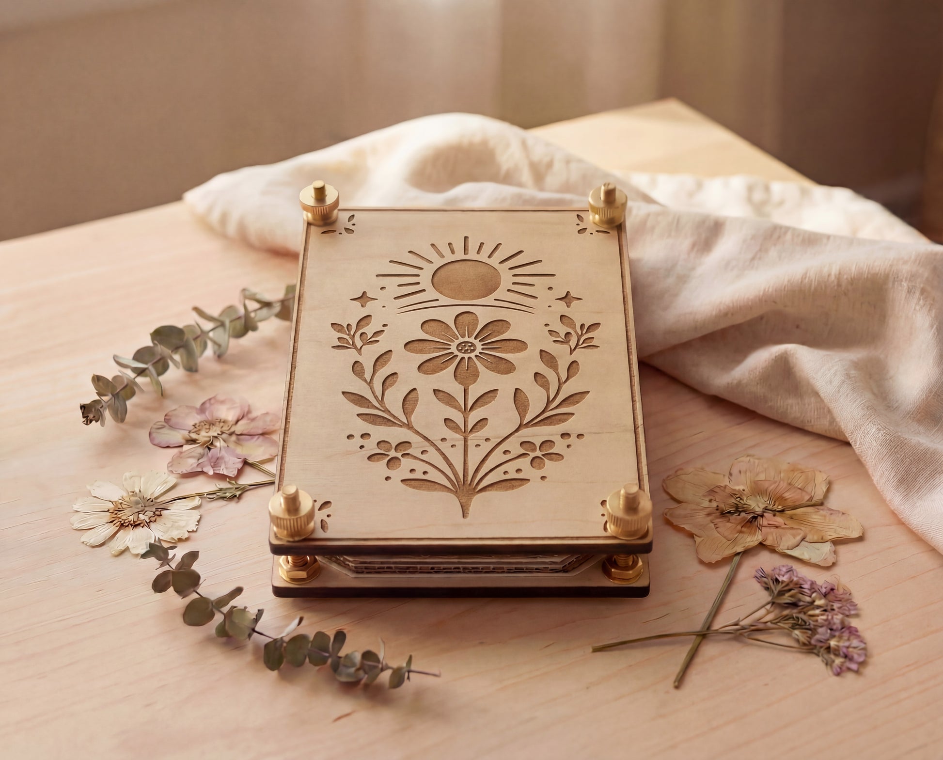 Handmade 4x6 maple wooden flower press kit with engraved sun and wildflower botanical design and brass knurled thumb nuts, styled on a light wood table with dried pressed flowers and eucalyptus, a portable pressed flower kit for beginners used to press wildflowers and leaves for botanical crafts, nature journaling, scrapbooking and pressed flower art.