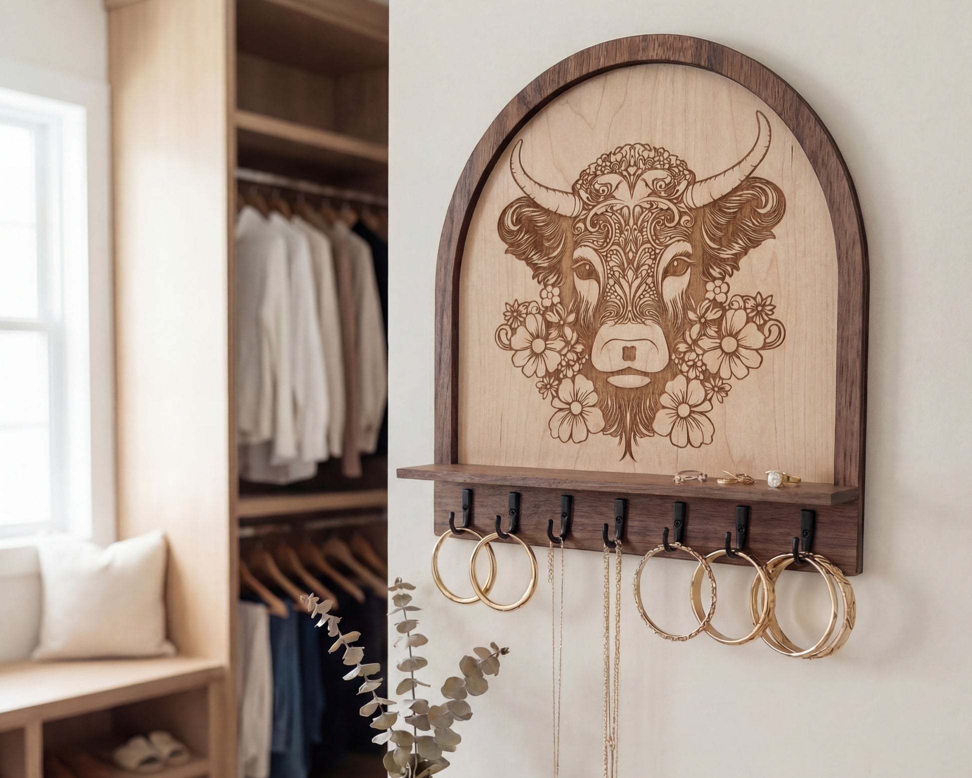 Laser engraved floral highland cow wood wall organizer with shelf and hooks, shown as a key and jewelry holder with hoop earrings and necklaces hanging in a neutral farmhouse-style entryway.