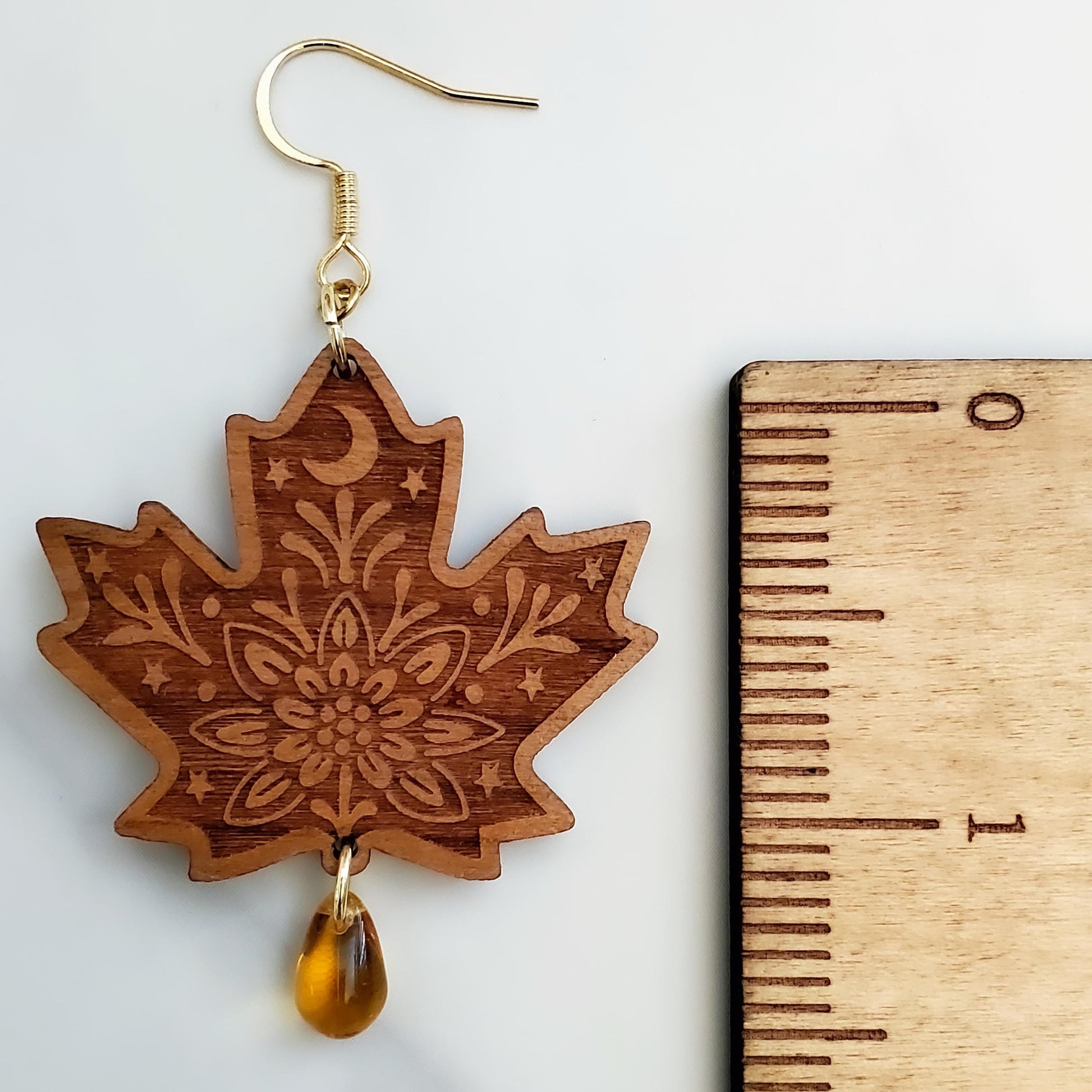 Close-up of engraved maple leaf wood dangle earring with amber Czech glass teardrop bead and 14k gold hook next to a ruler for size.
