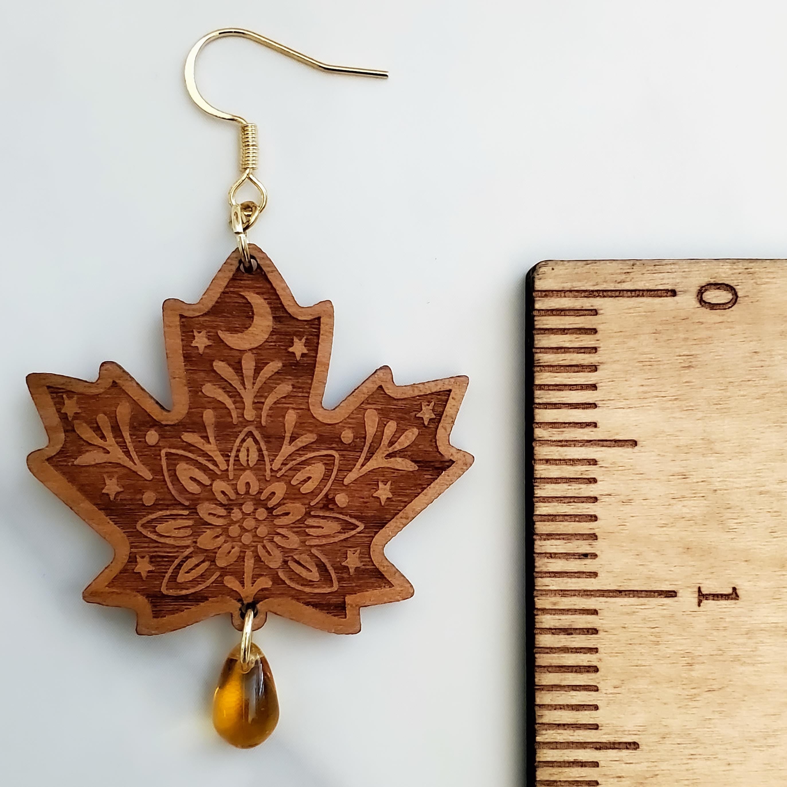 Close-up of engraved maple leaf wood dangle earring with amber Czech glass teardrop bead and 14k gold hook next to a ruler for size.