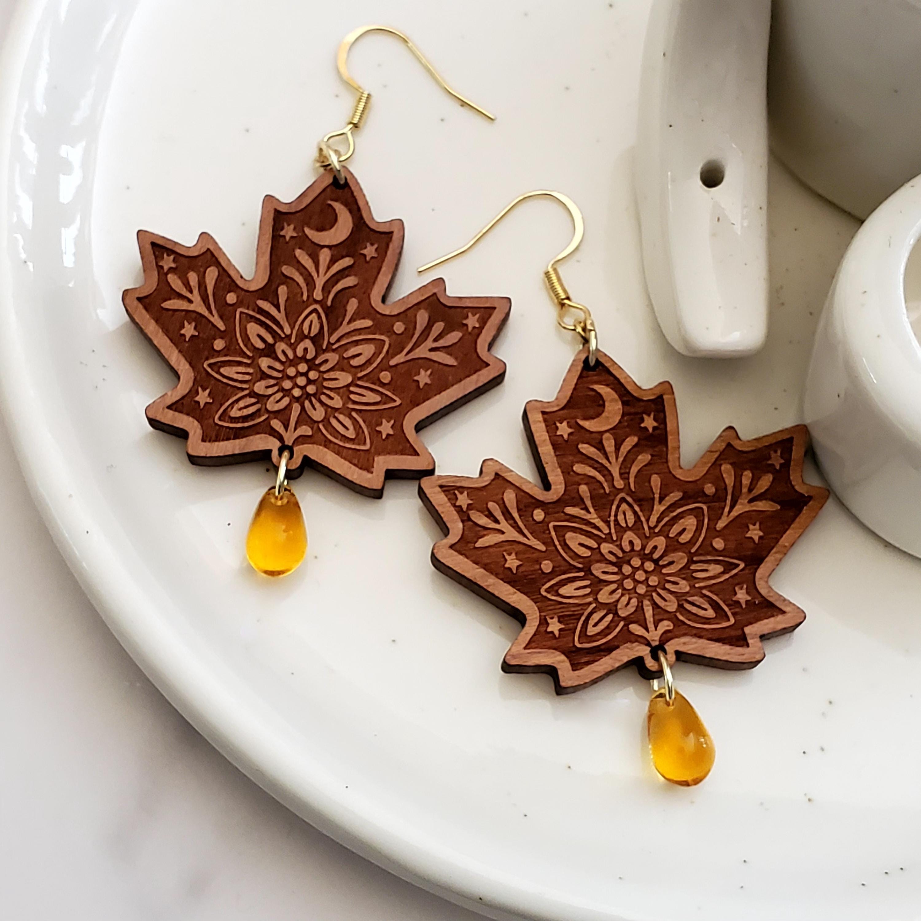 Pair of engraved maple leaf wood dangle earrings with amber Czech glass teardrop beads and 14k gold hooks on a ceramic tray.