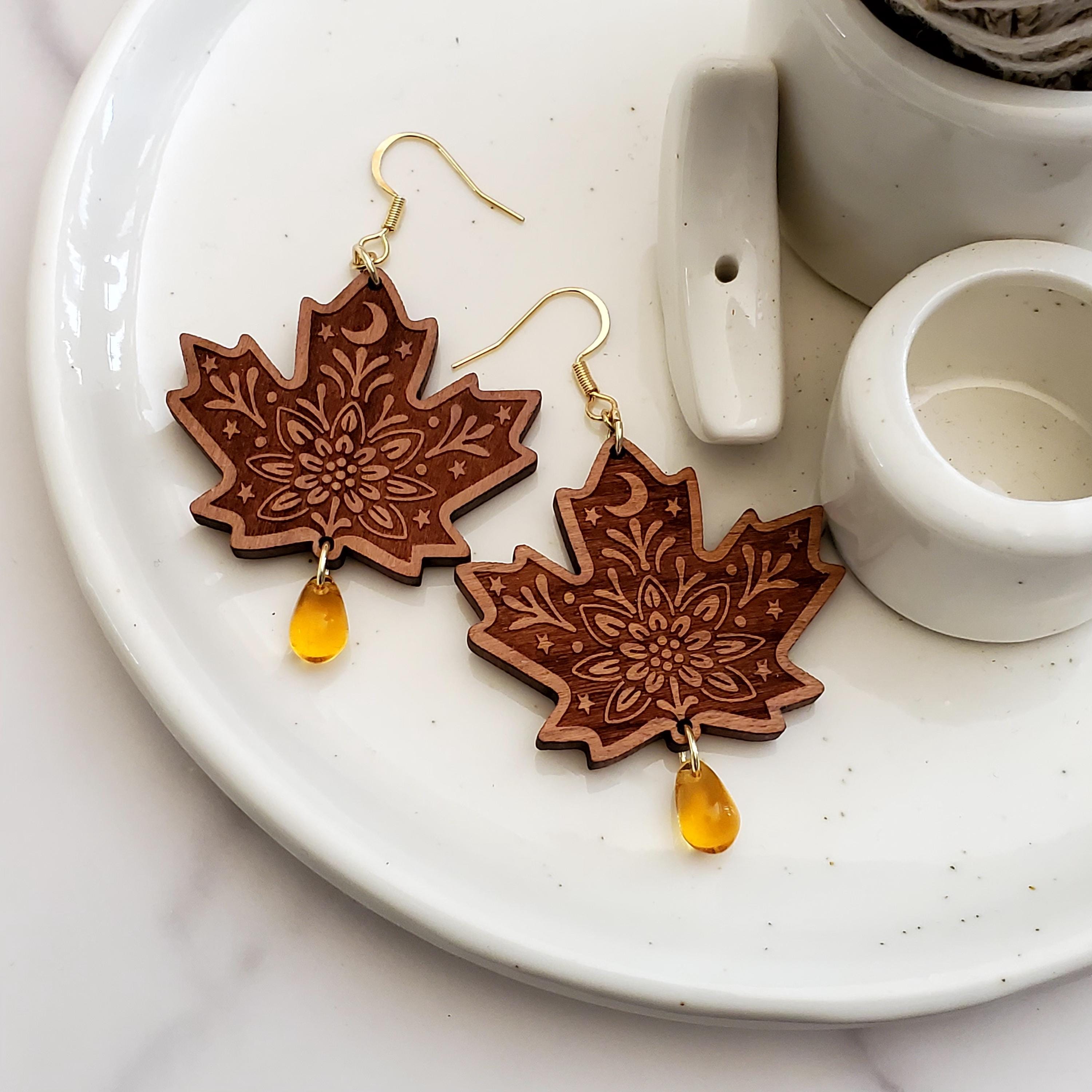 Pair of engraved maple leaf wood dangle earrings with amber Czech glass teardrop beads and 14k gold hooks on a ceramic tray.