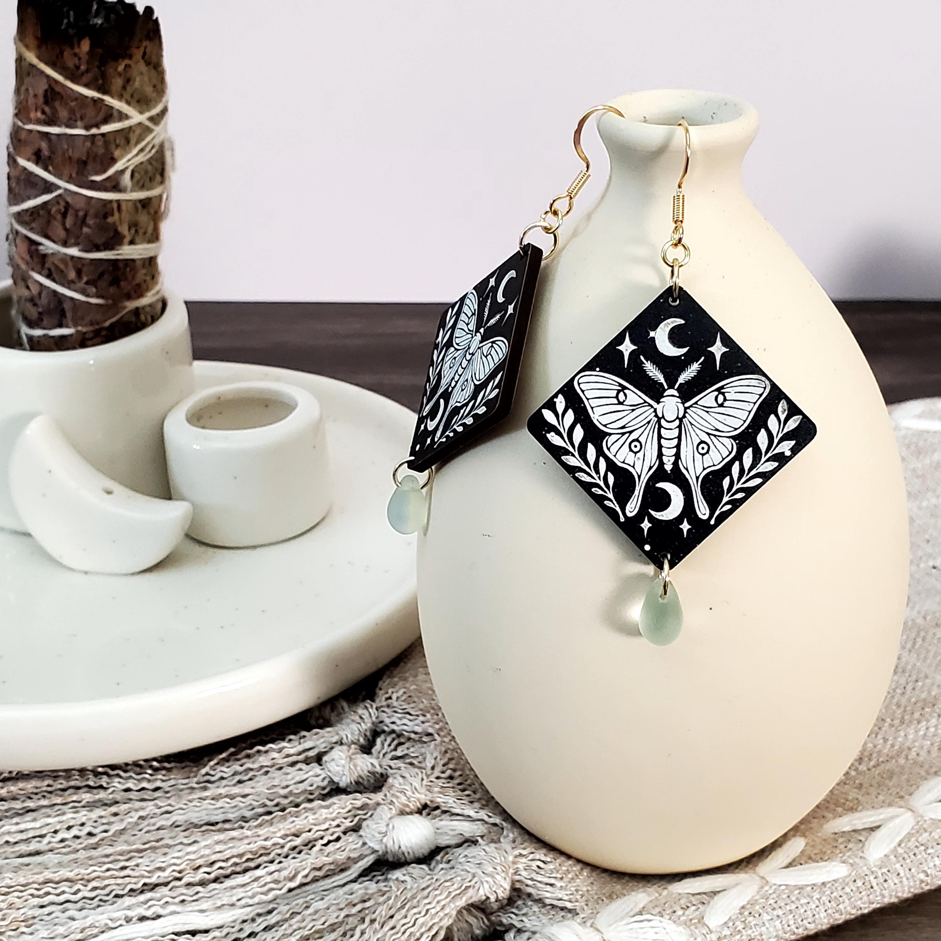 Engraved moth diamond wood dangle earrings with crescent moon details, mint Czech glass teardrop beads, and 14k gold hooks displayed on a ceramic vase.