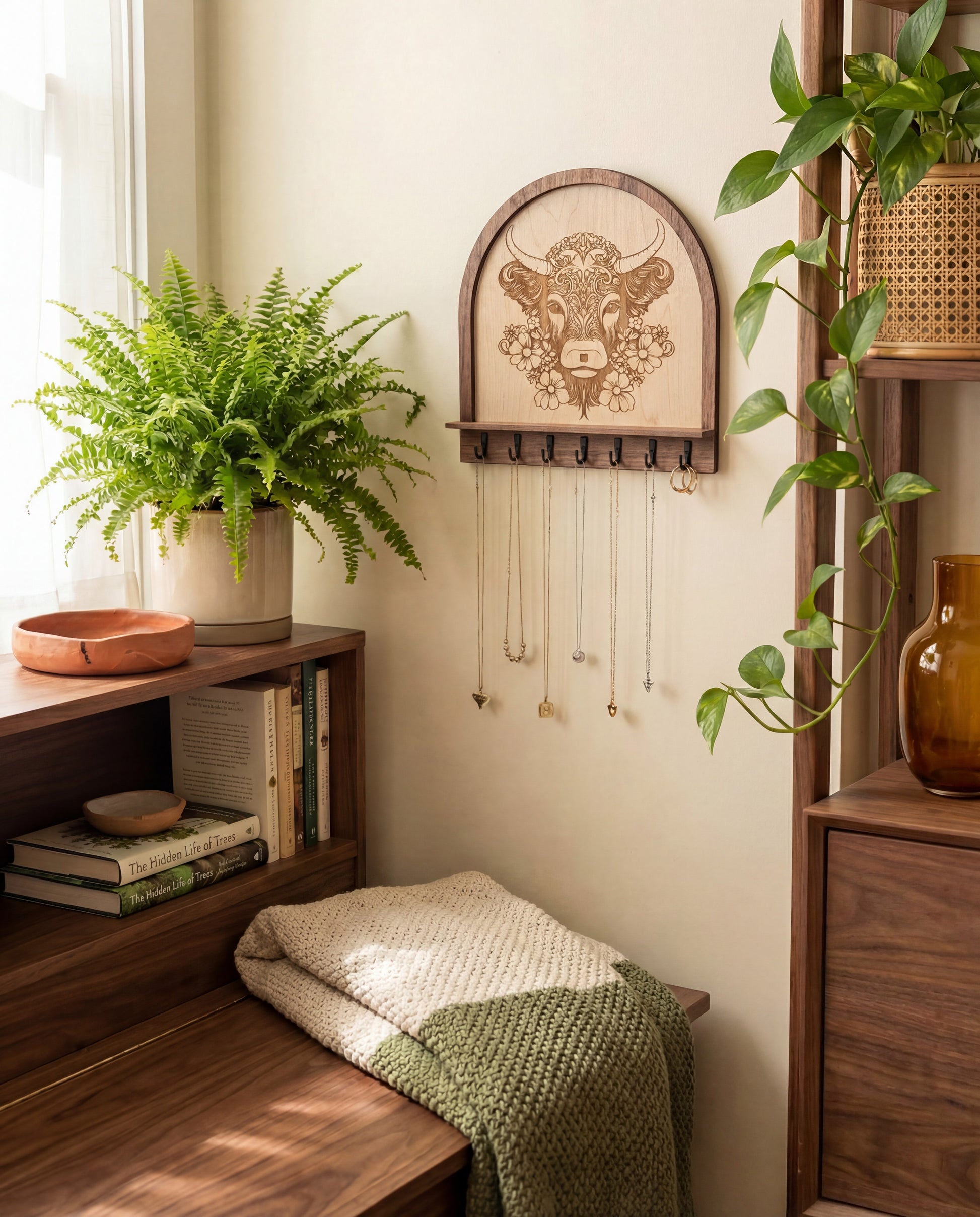 Laser engraved floral highland cow wood wall organizer with shelf and hooks, styled as a key and jewelry holder with necklaces hanging in a cozy boho farmhouse nook with plants and wooden shelving.