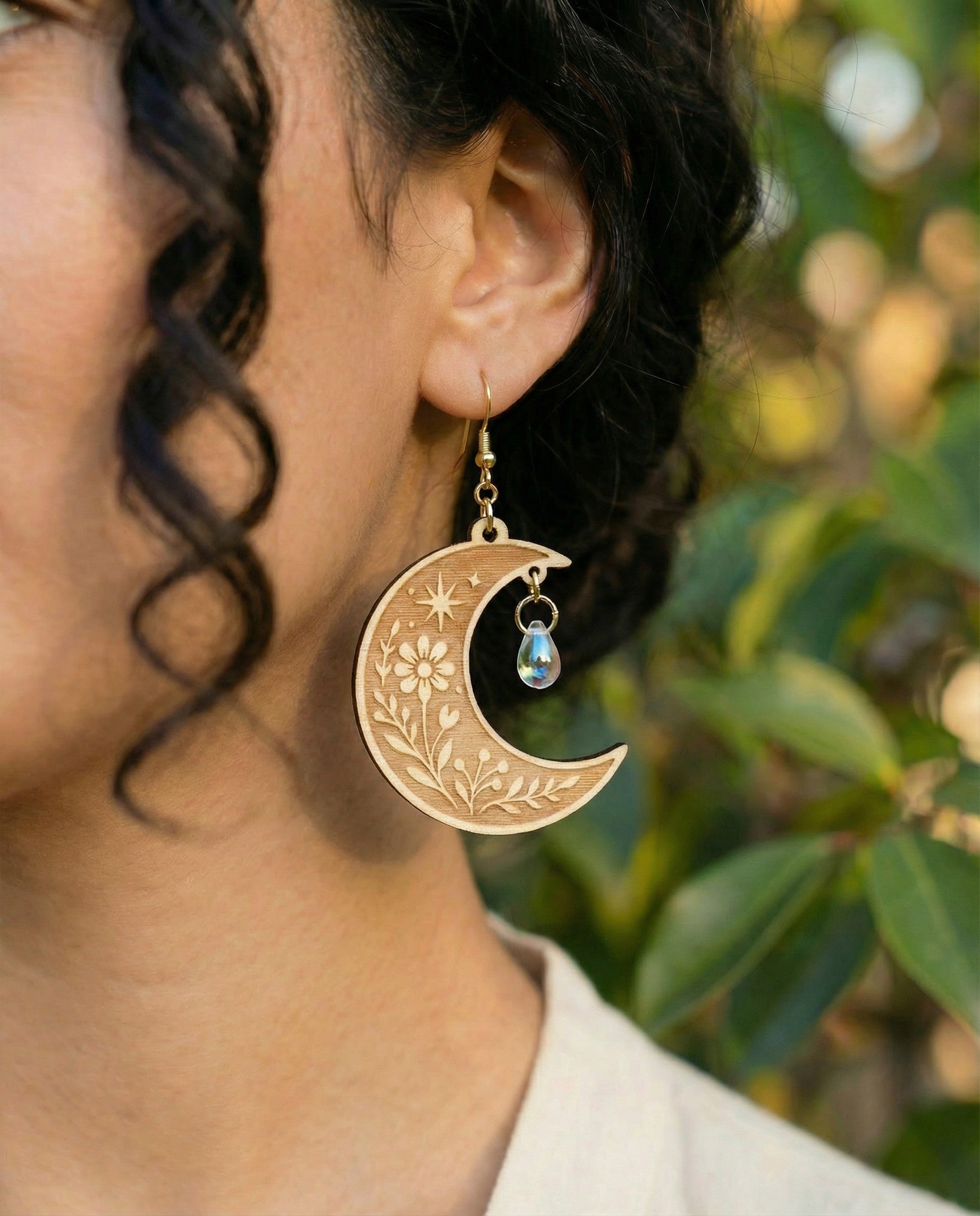 Gold crescent moon earring with floral design and pearl accent worn by a person outdoors.