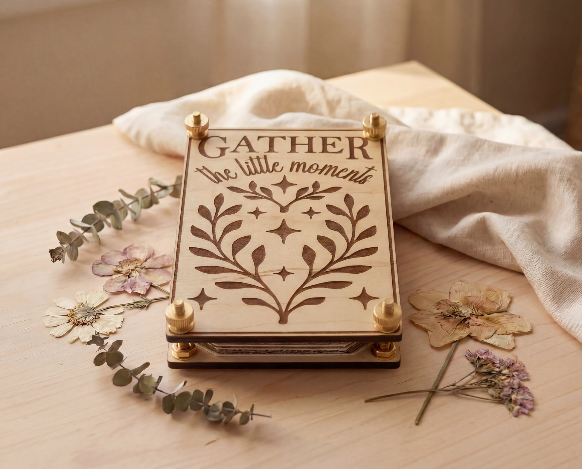 Handmade 4x6 maple flower press with brass hardware and original “Gather the little moments” engraved design, photographed on a light wood surface with linen cloth, eucalyptus sprigs, and pressed flowers.