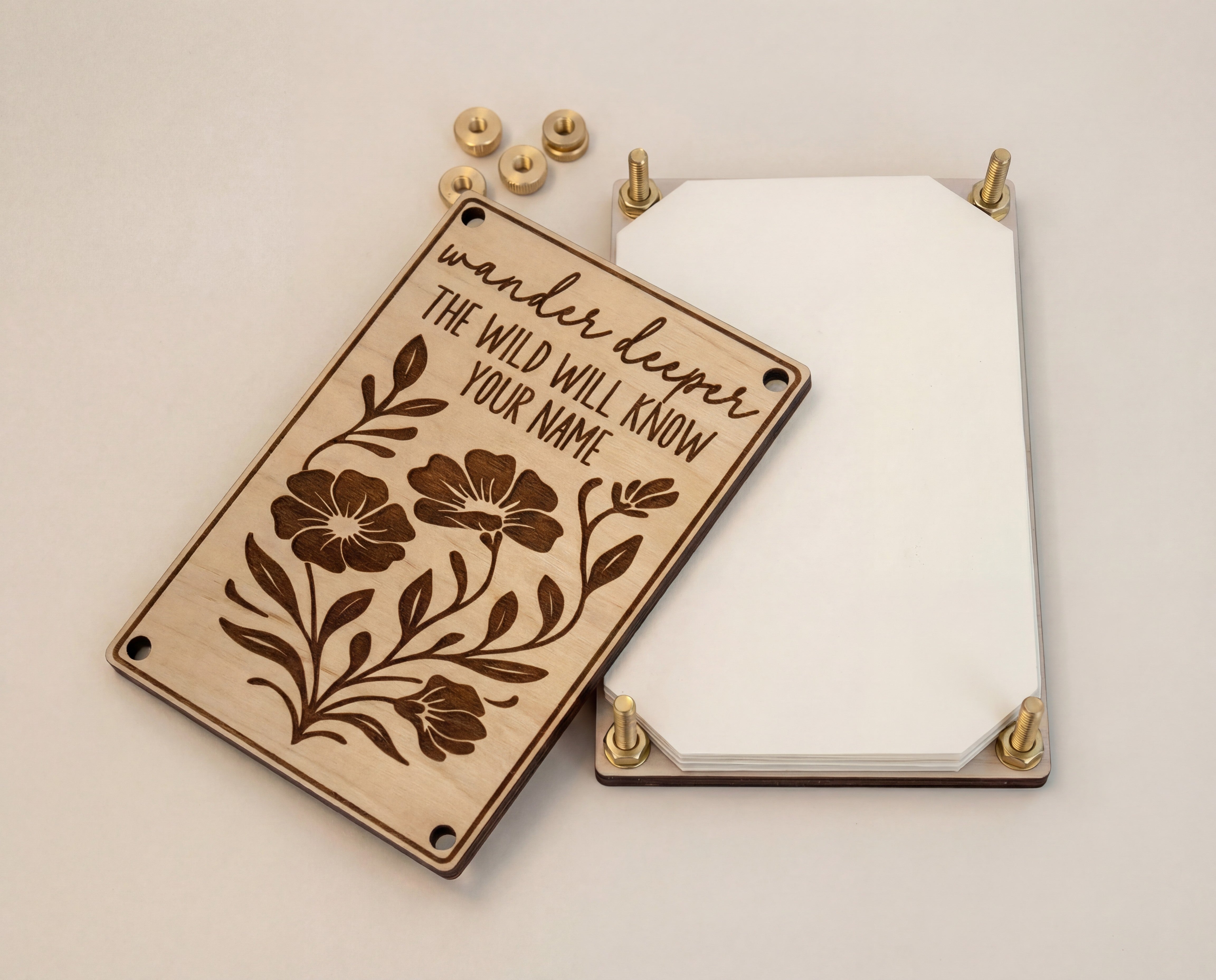 Handmade 4x6 maple flower press kit with “Wander deeper, the wild will know your name” engraved top plate, brass bolts and knurled thumb nuts, and stacked blotting paper shown separated on a clean white background.