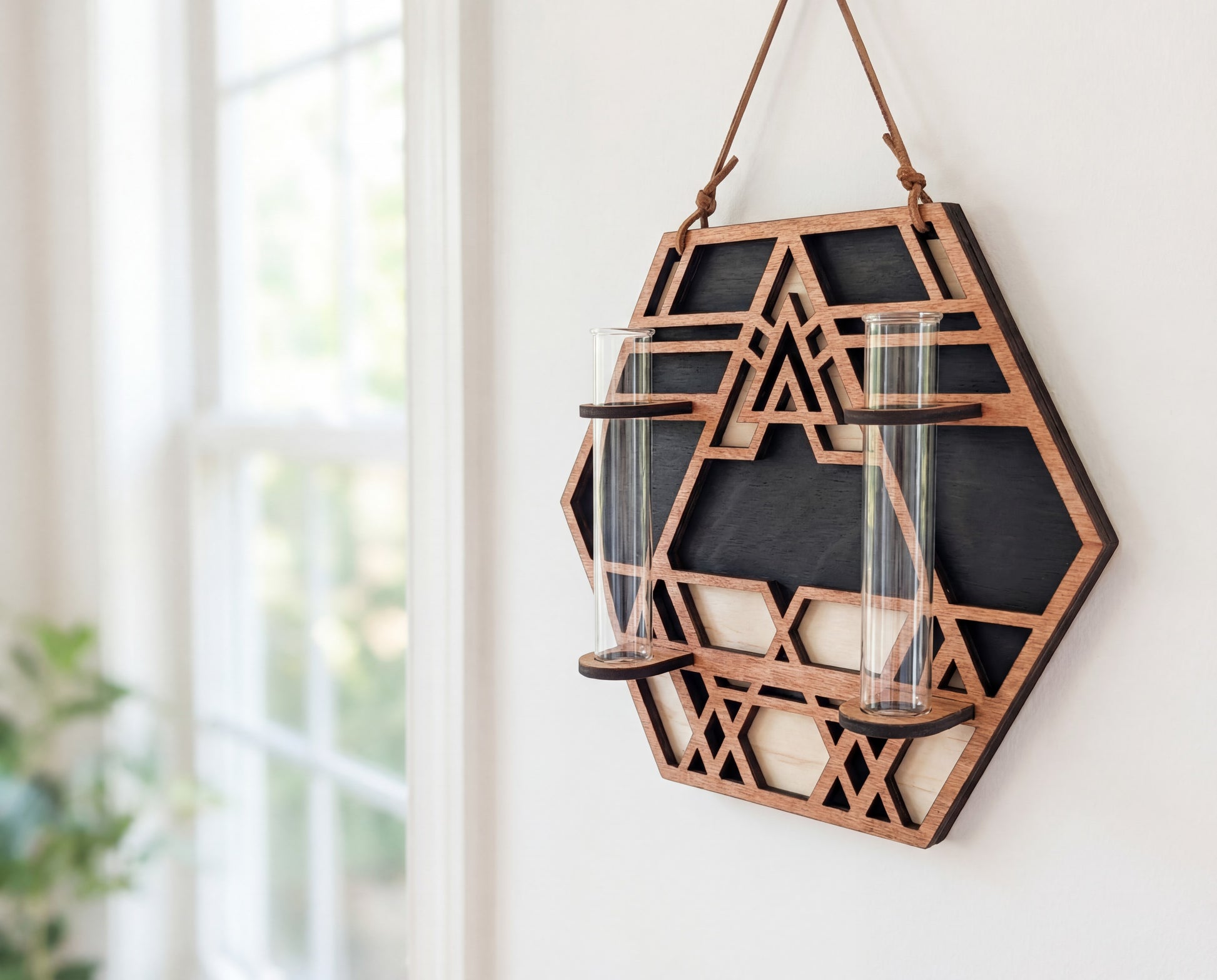 Side view of a geometric hexagon wall propagation station made from three-layer maple veneer MDF, featuring a sacred geometry cutout design, suede hanging strap, and two 6.25-inch by 1-inch glass vials for water propagating plant cuttings near a bright window.