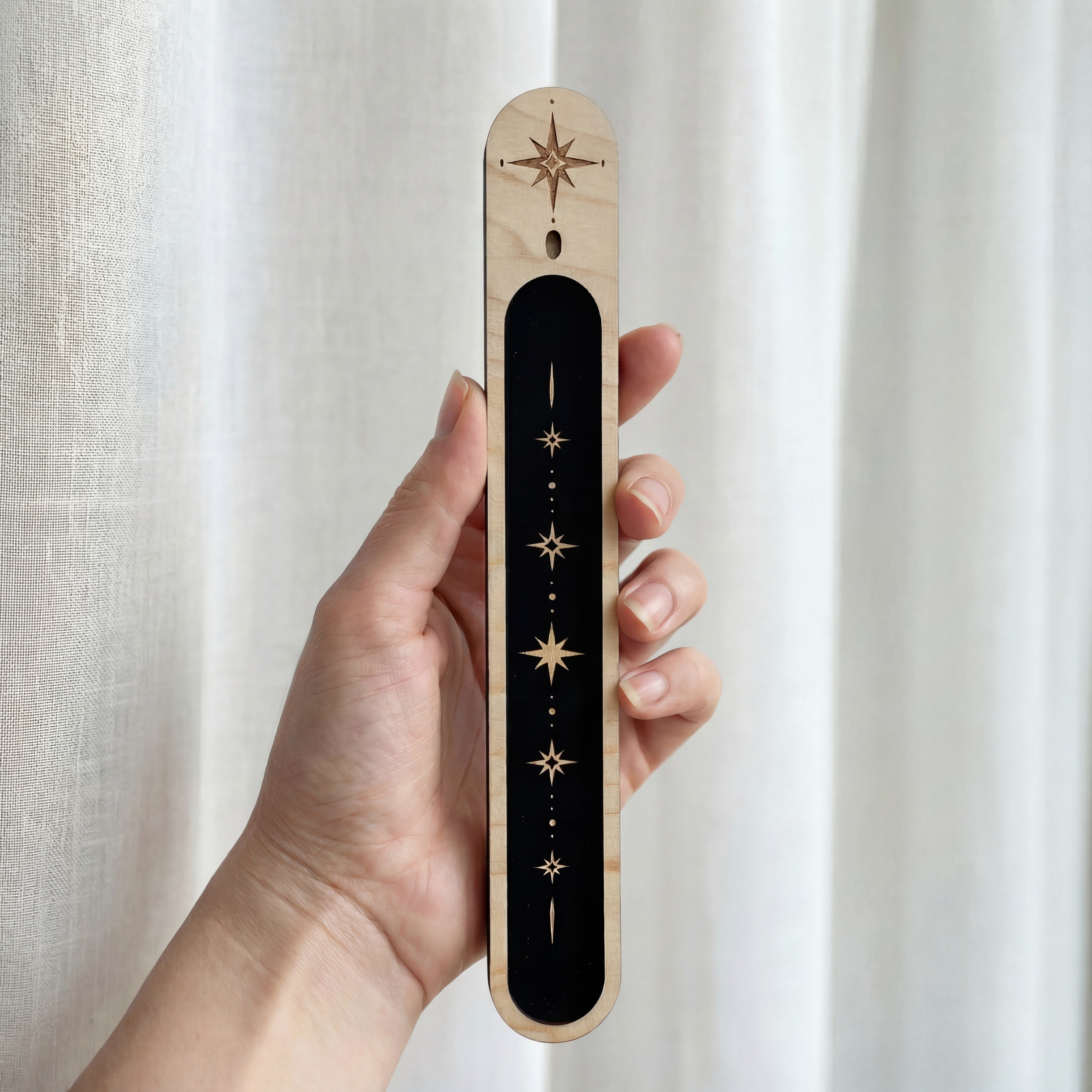 Hand holding a slim wooden incense holder with a black inlay and gold celestial star design.