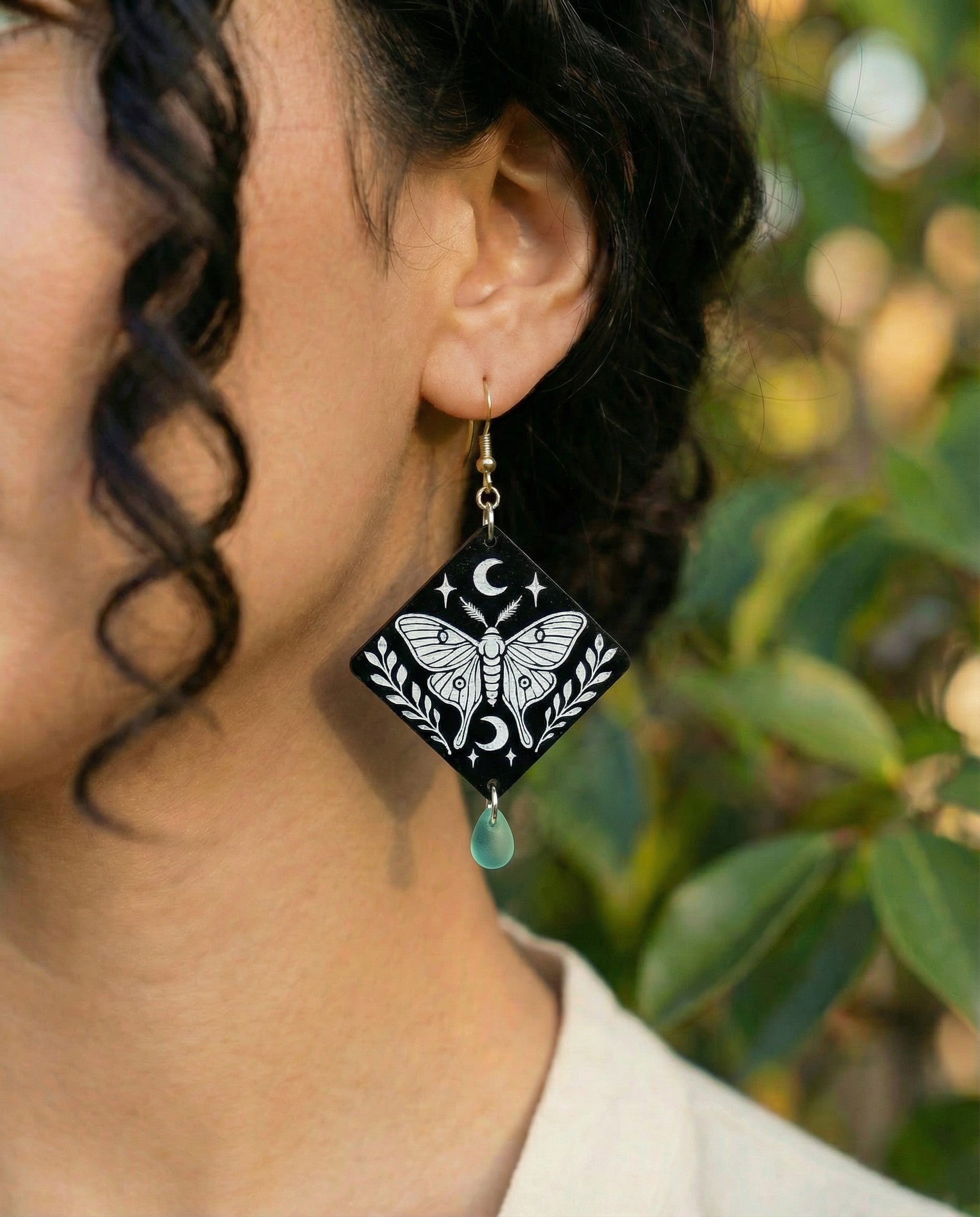 Model wearing engraved moth diamond wood dangle earring with crescent moon design, mint Czech glass teardrop bead, and 14k gold hook.