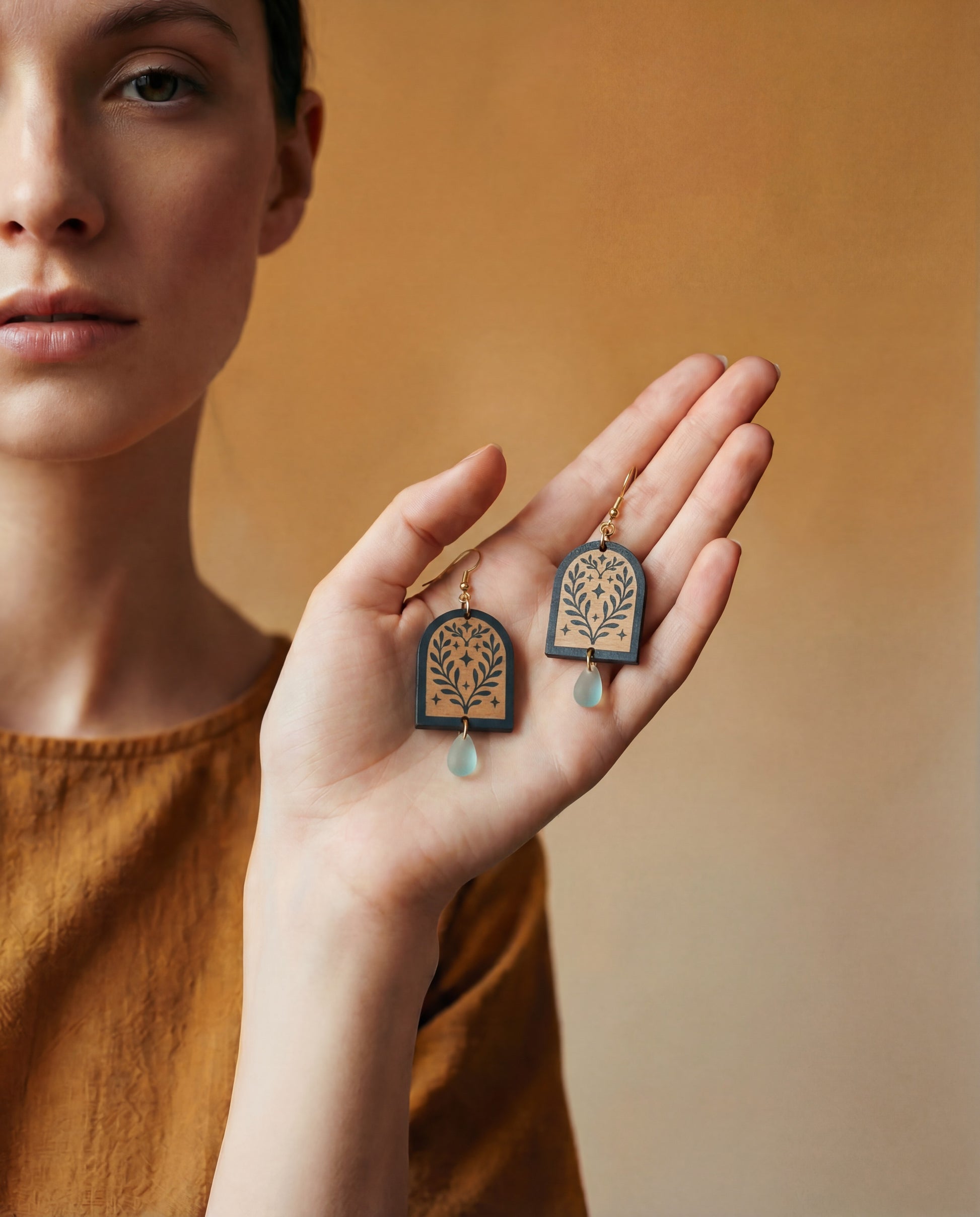 Person holding a pair of decorative earrings with a neutral background