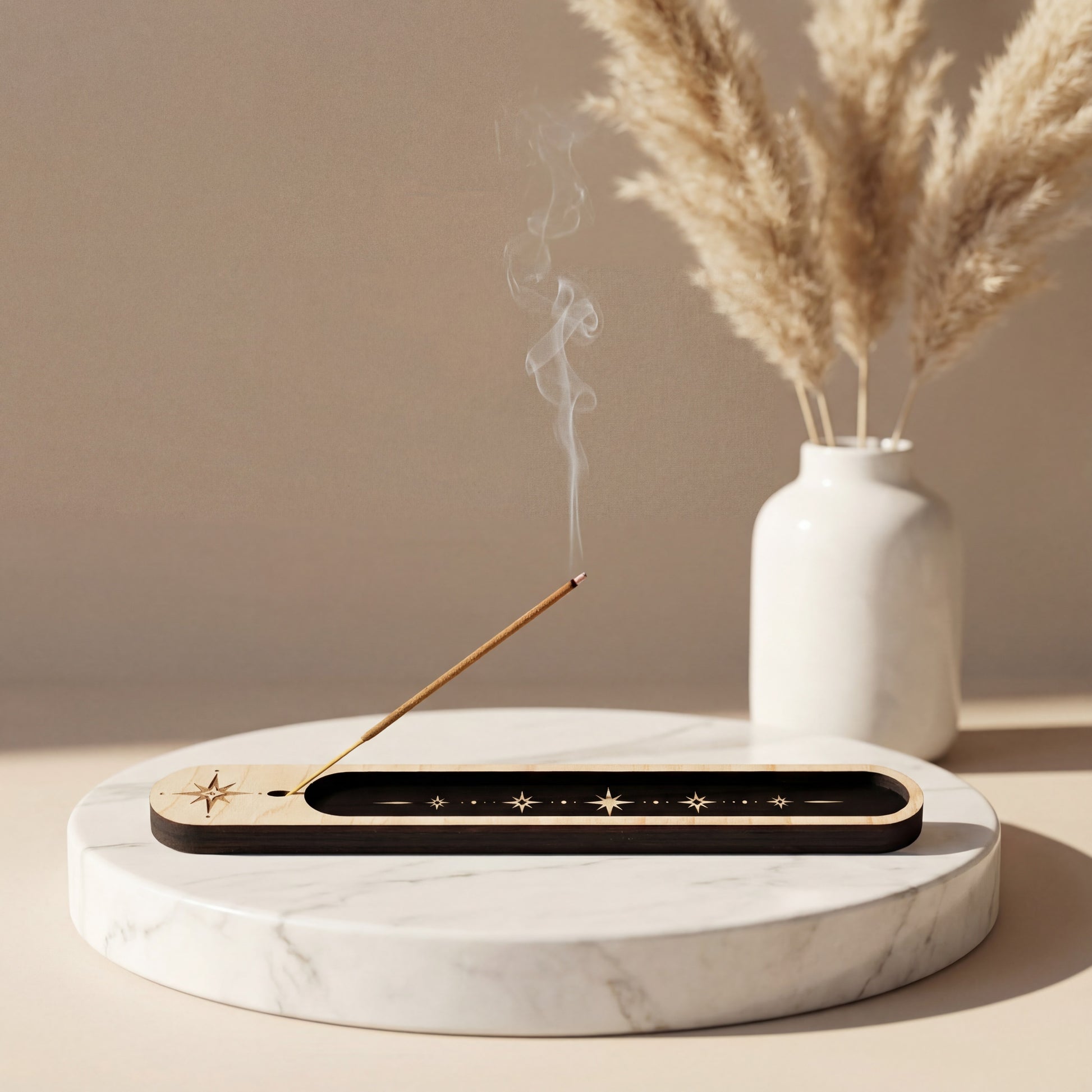 Lit incense stick in a wooden celestial incense holder with black inlay and star design on a marble tray, with smoke rising beside a white vase.