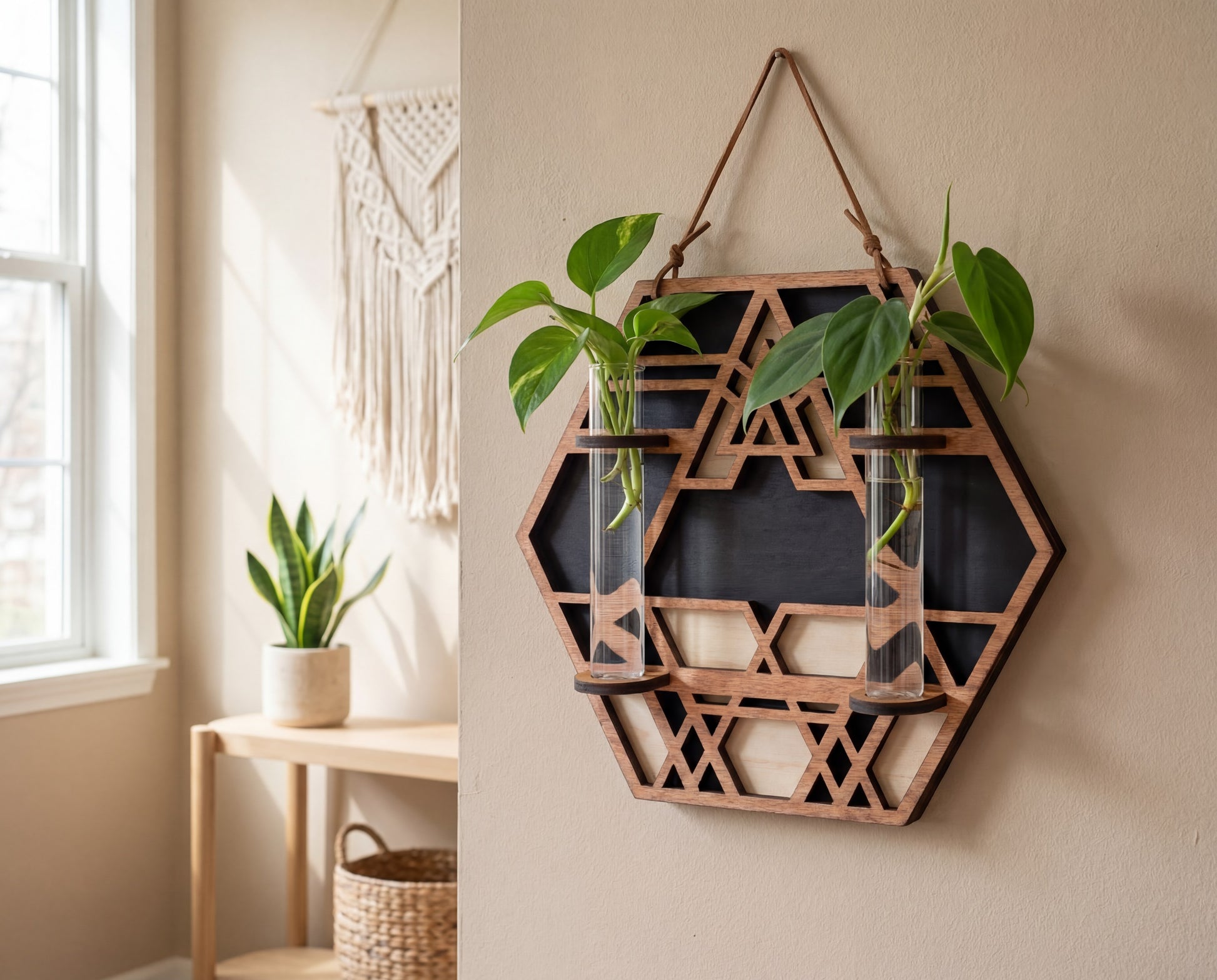 Geometric hexagon wall propagation station in layered maple veneer MDF with sacred geometry cutout pattern, suede hanging strap, and two 6.25-inch by 1-inch glass vials holding pothos cuttings, styled as modern boho plant wall decor in a bright room.