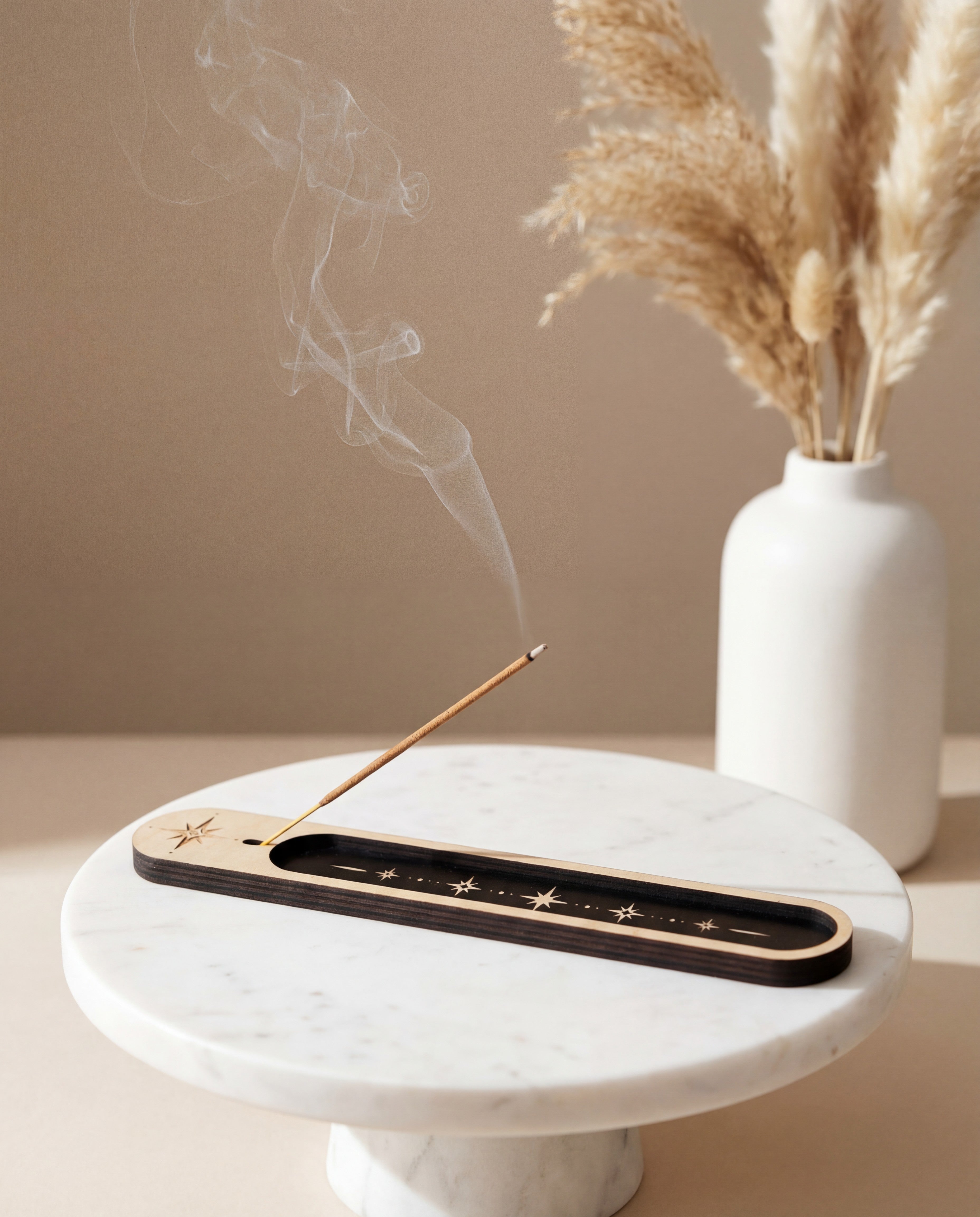 Lit incense stick in a wooden celestial incense holder with black inlay and star design on a marble tray, with smoke rising beside a white vase.