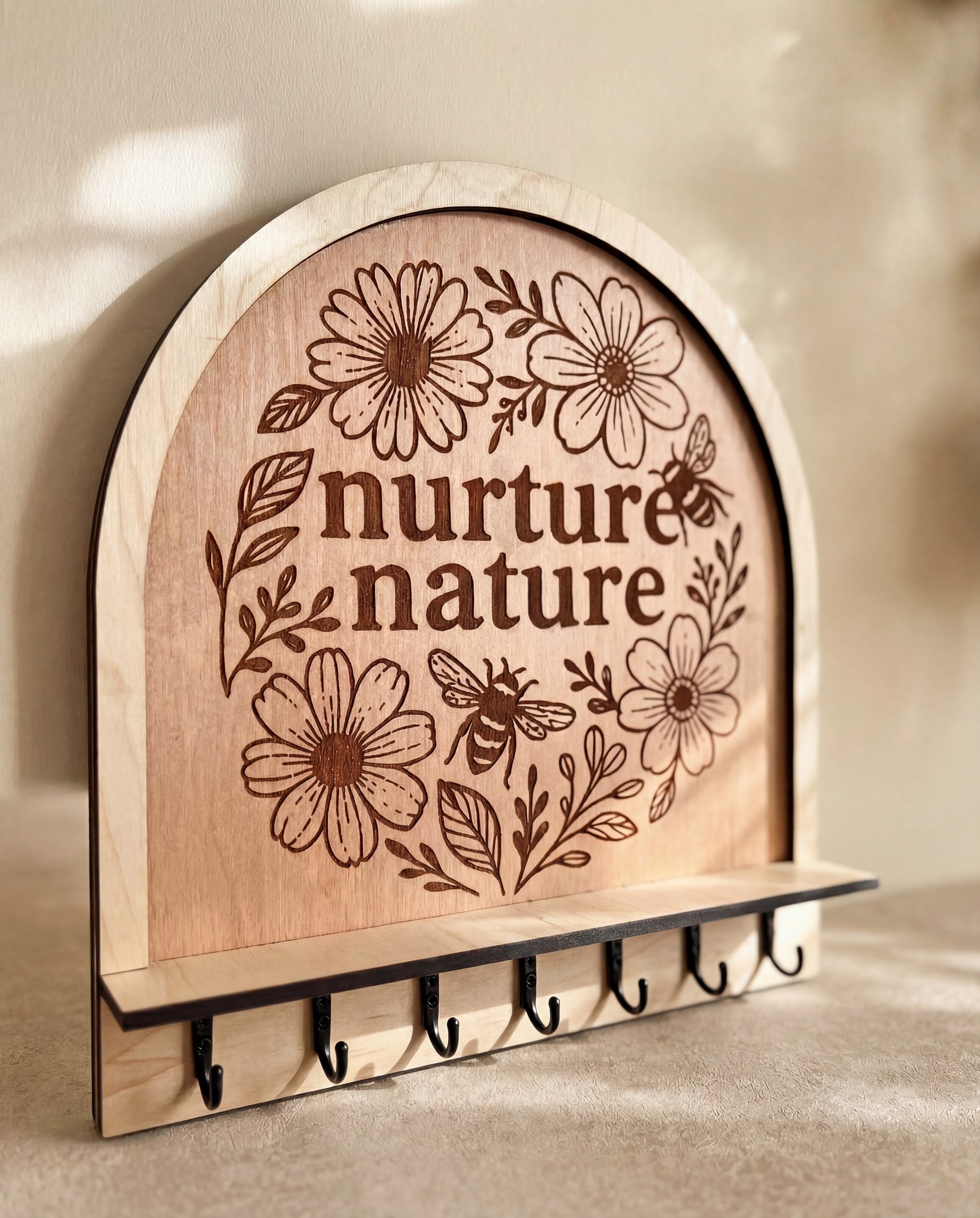 “Nurture nature” engraved wooden key holder with floral design, bee illustration, and a row of hooks.