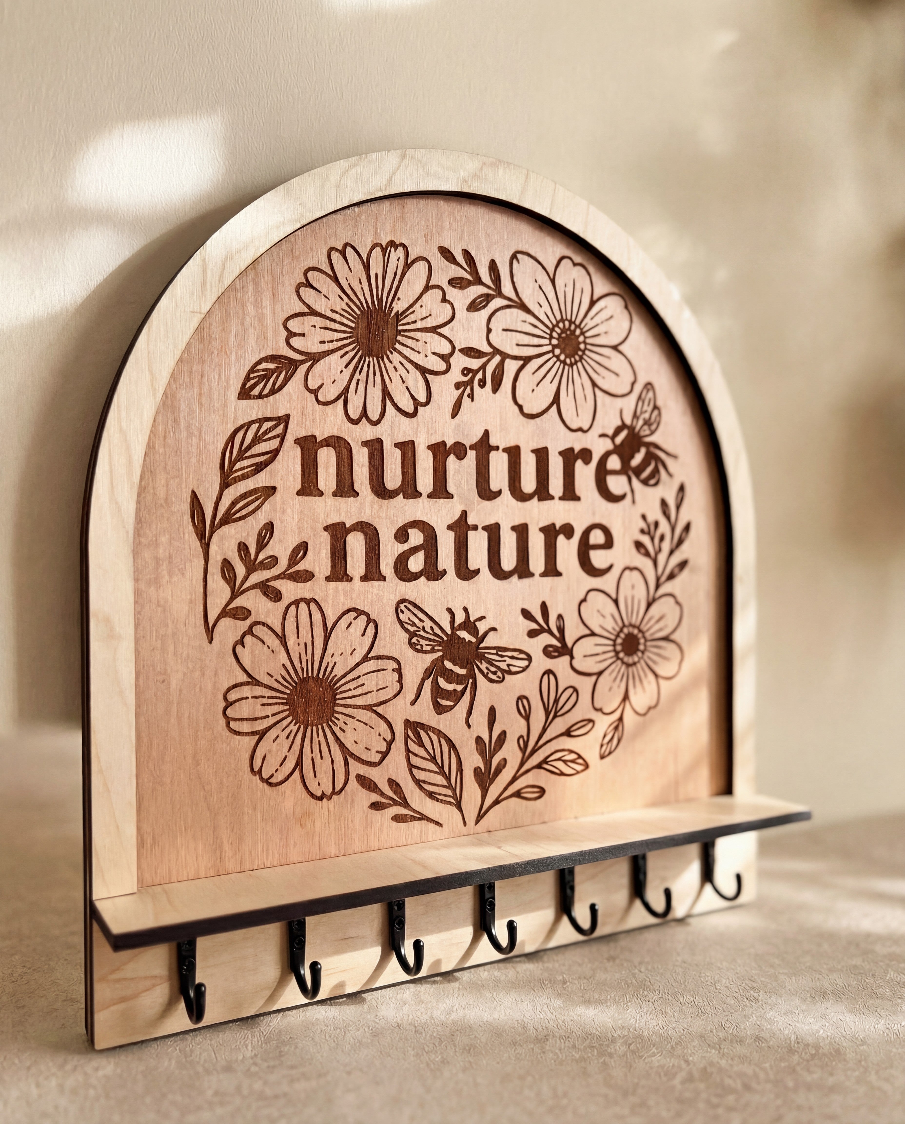 “Nurture nature” engraved wooden key holder with floral design, bee illustration, and a row of hooks.