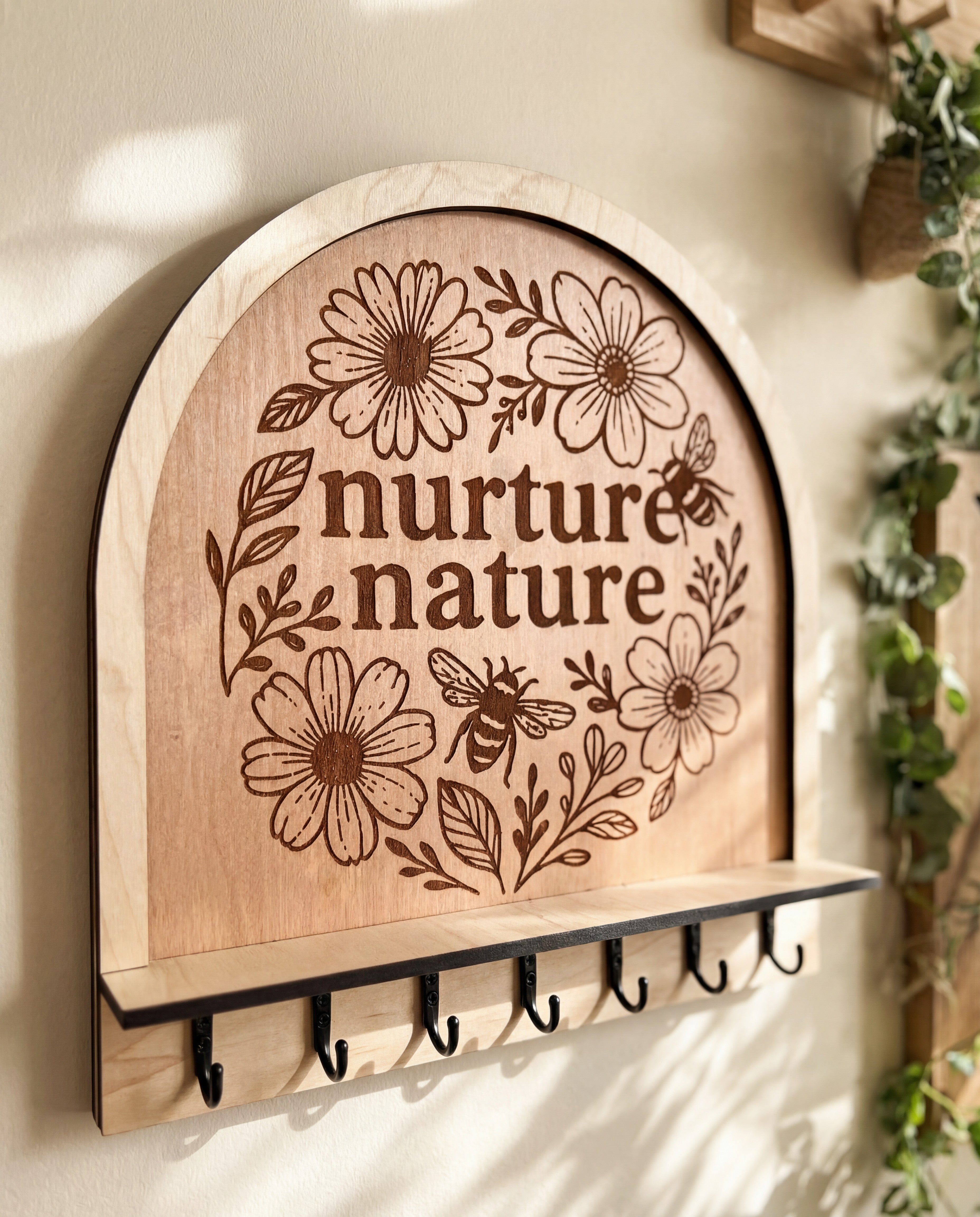 Arched wooden wall hook rack with “nurture nature” floral bee engraving and 7 black metal hooks.