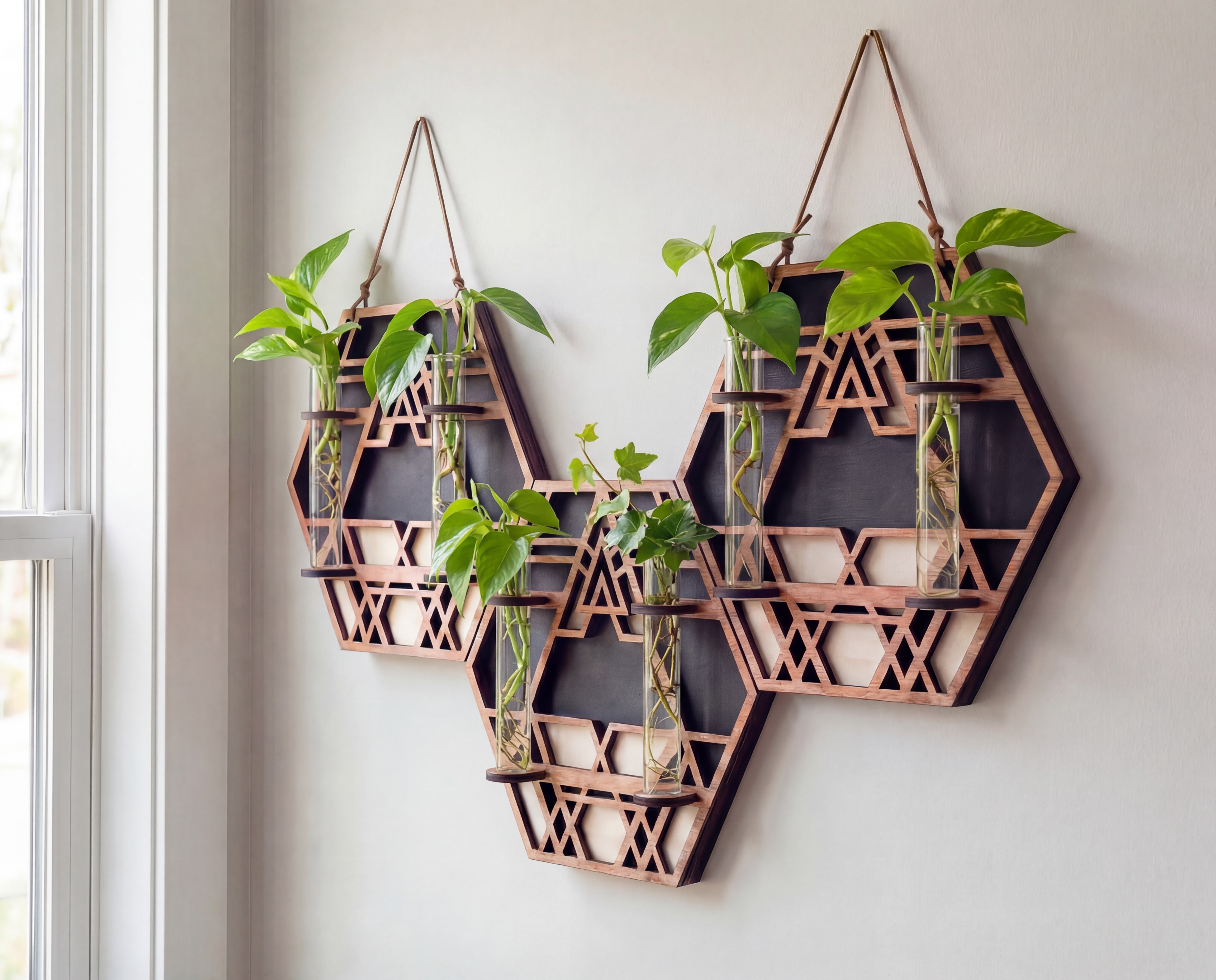 XL trio geometric wall propagation station in layered maple veneer MDF with sacred geometry cutout design, three connected hexagon panels, suede hanging straps, and six 6.25-inch by 1-inch glass vials holding pothos cuttings, styled as modern boho plant wall decor near a window.