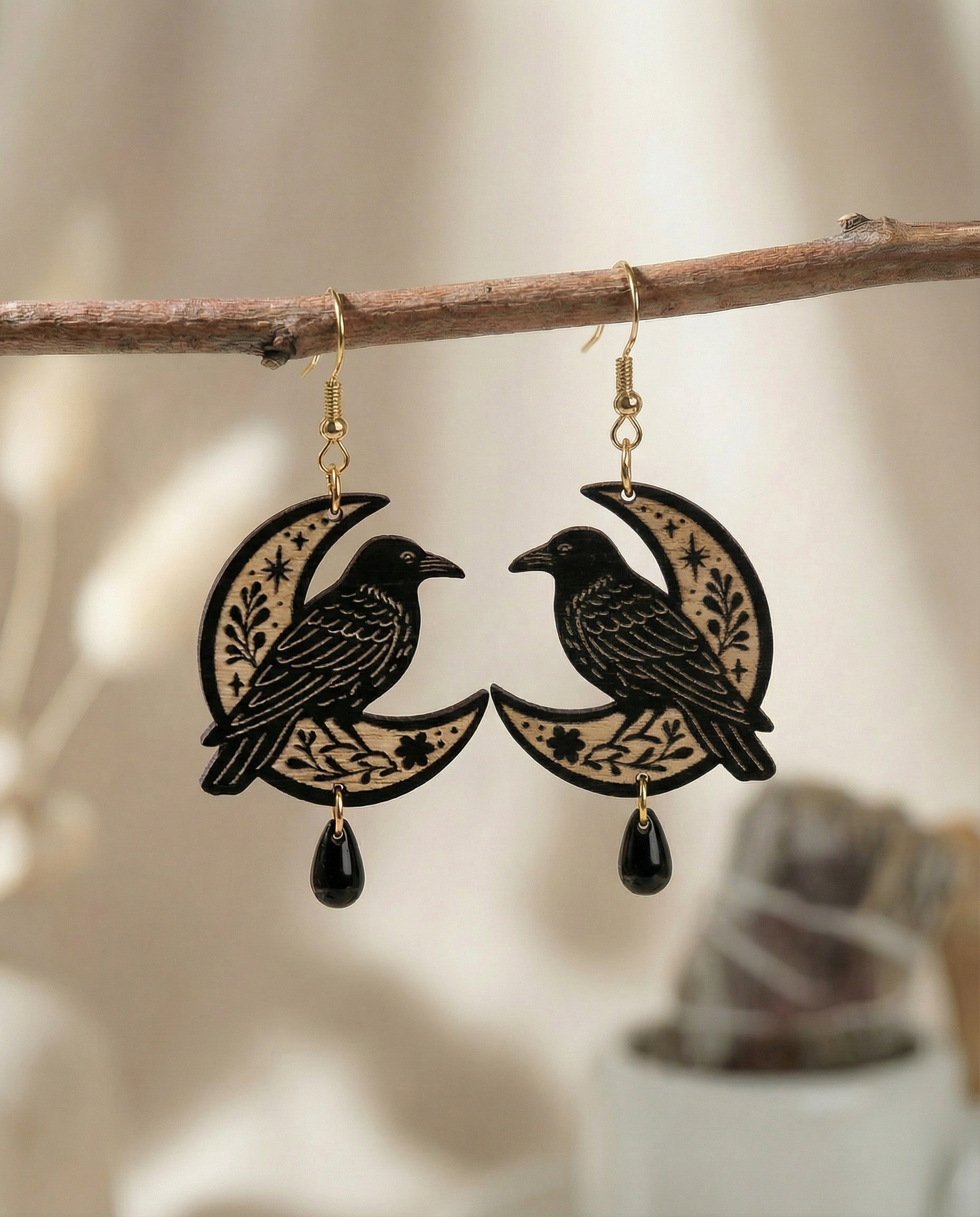 Pair of earrings with crow design on a branch against a blurred background