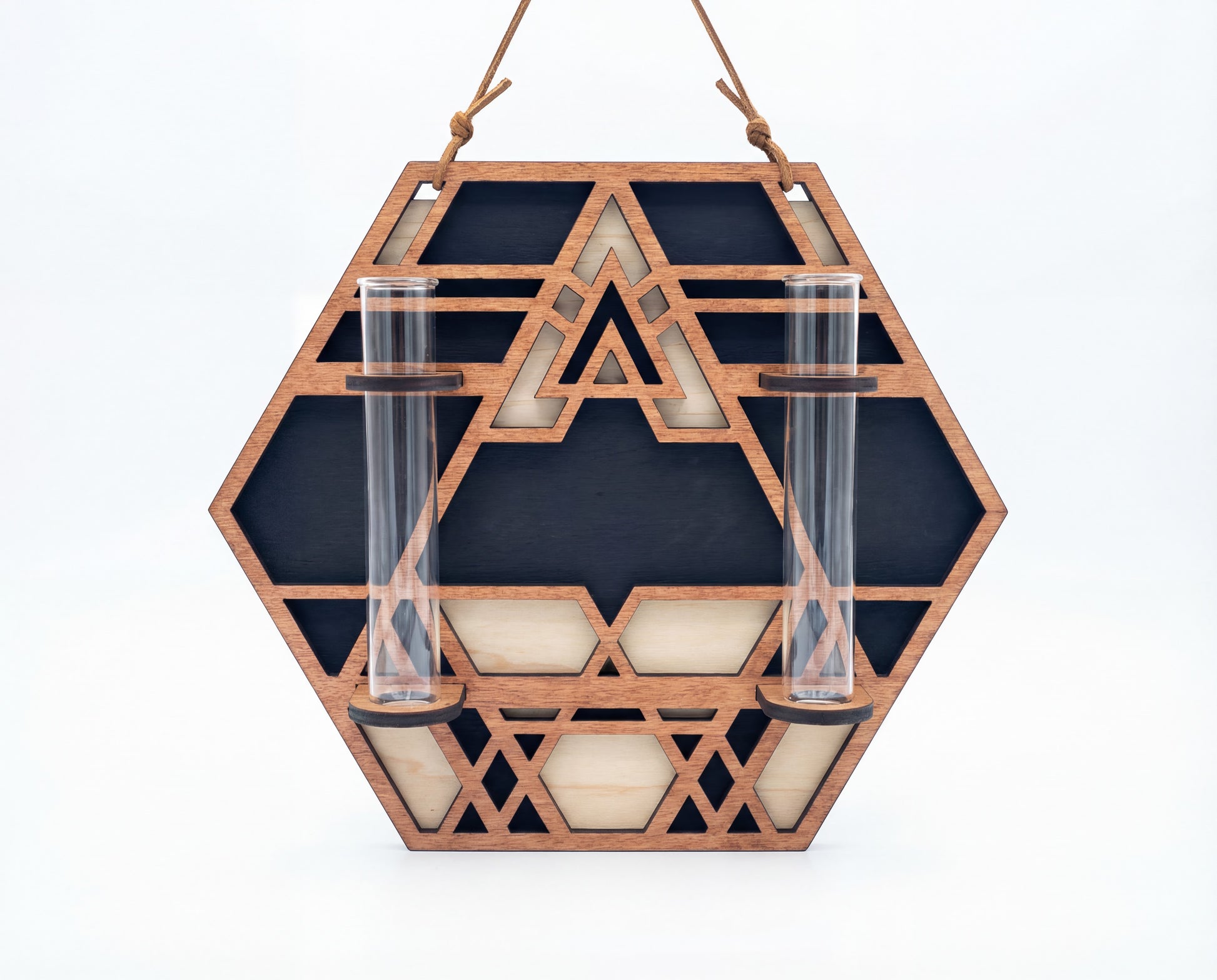 Front view of a geometric hexagon wall propagation station made from three-layer maple veneer MDF with sacred geometry cutout pattern, suede hanging strap, and two 6.25-inch by 1-inch clear glass vials for propagating plant cuttings on a white background.