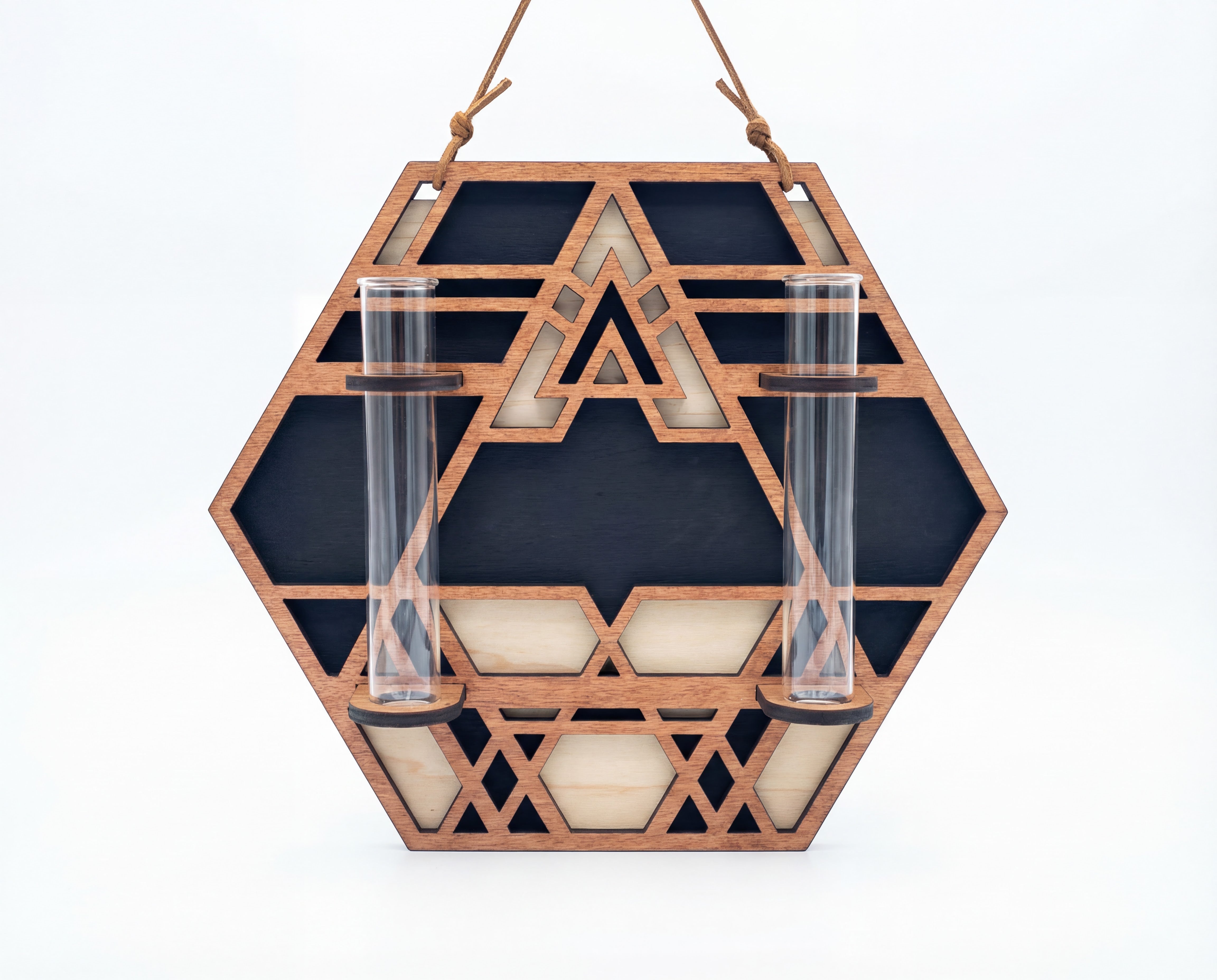 Front view of a geometric hexagon wall propagation station made from three-layer maple veneer MDF with sacred geometry cutout pattern, suede hanging strap, and two 6.25-inch by 1-inch clear glass vials for propagating plant cuttings on a white background.
