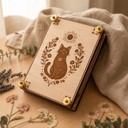 Handcrafted wooden flower press featuring an engraved black cat surrounded by delicate botanical florals and a sun motif. Finished with brass hardware and styled against soft natural linen, dried lavender, eucalyptus, and pressed flowers on a warm wooden surface.
