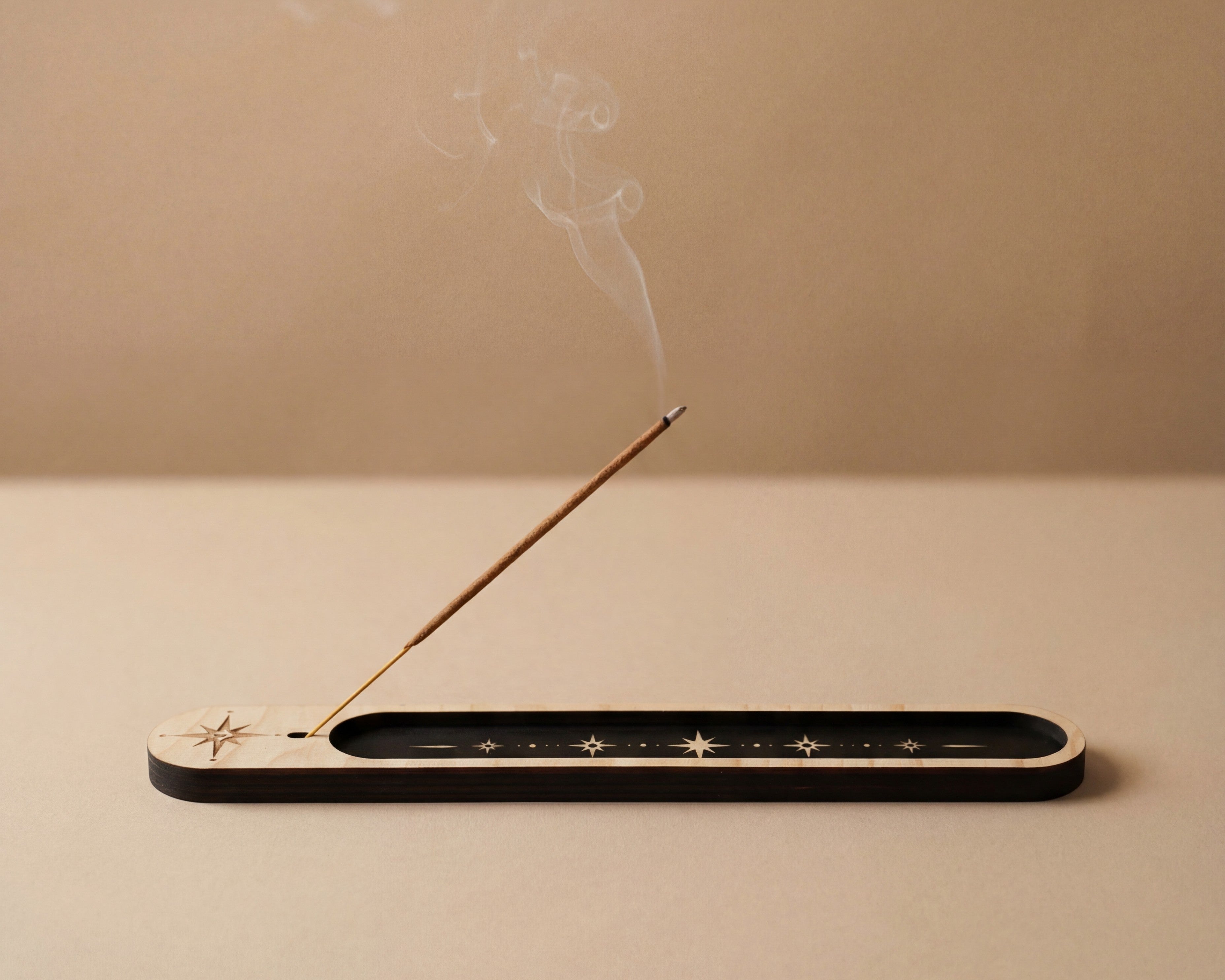 Lit incense stick resting in a slim wooden celestial incense holder with black inlay and star details, with smoke drifting upward.